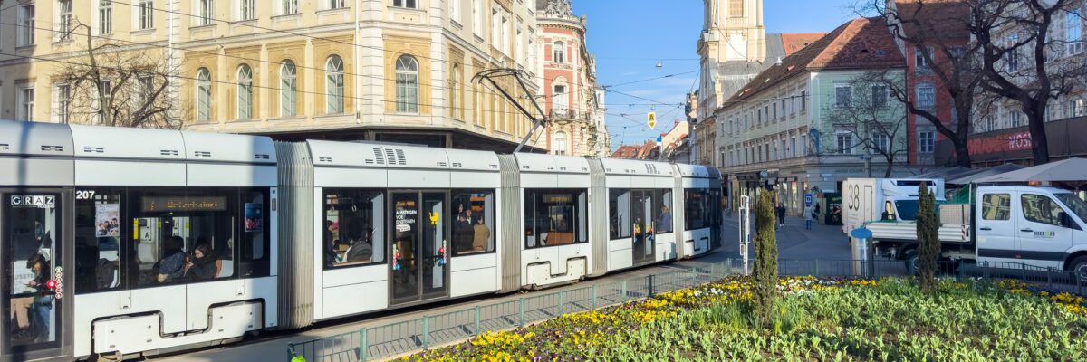 Eine Straßenbahn fährt am Eisernen Tor in Graz vorbei, im Vordergrund ein Blumenbeet.