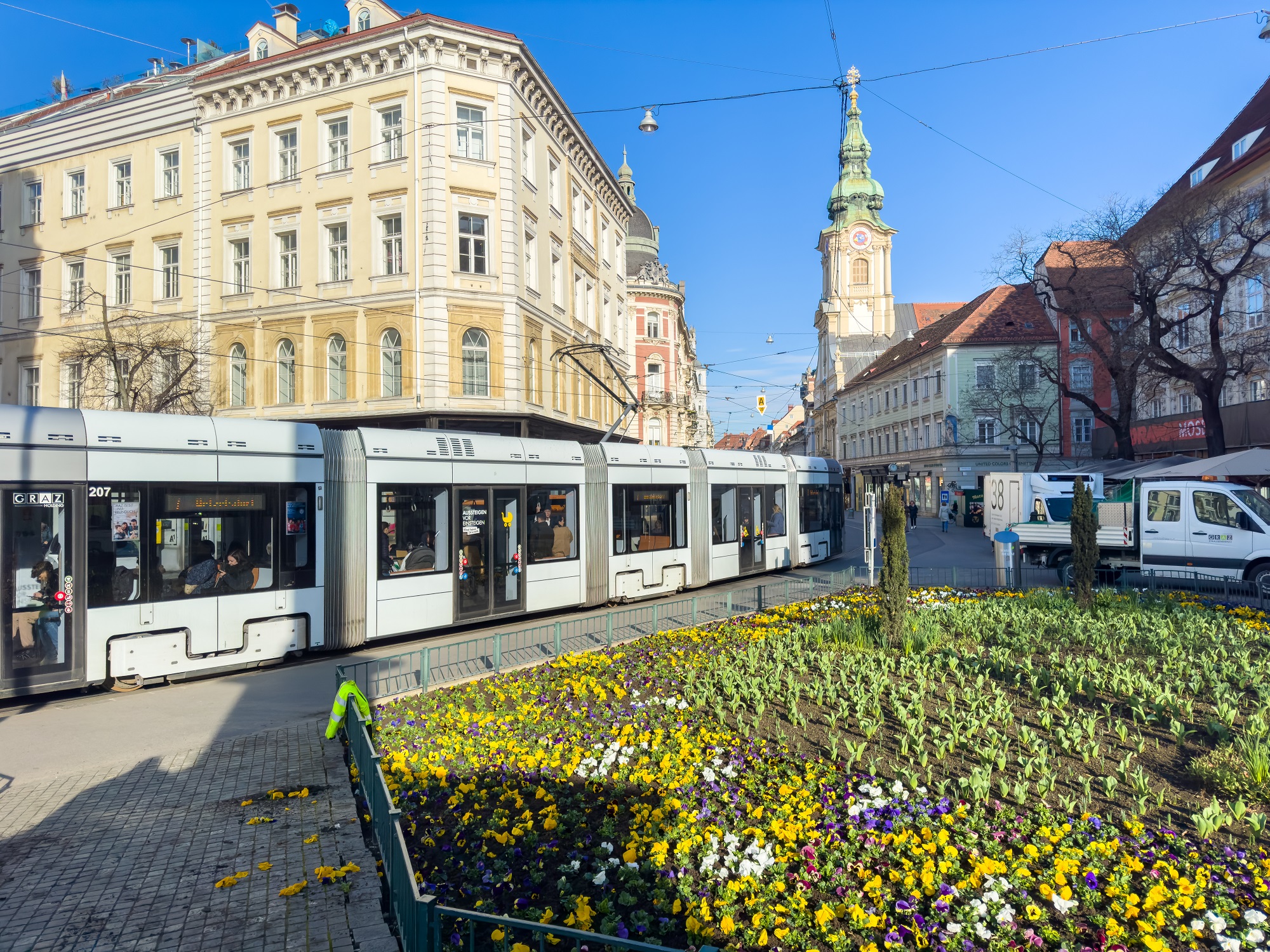 Eine Straßenbahn fährt am Eisernen Tor in Graz vorbei, im Vordergrund ein Blumenbeet.