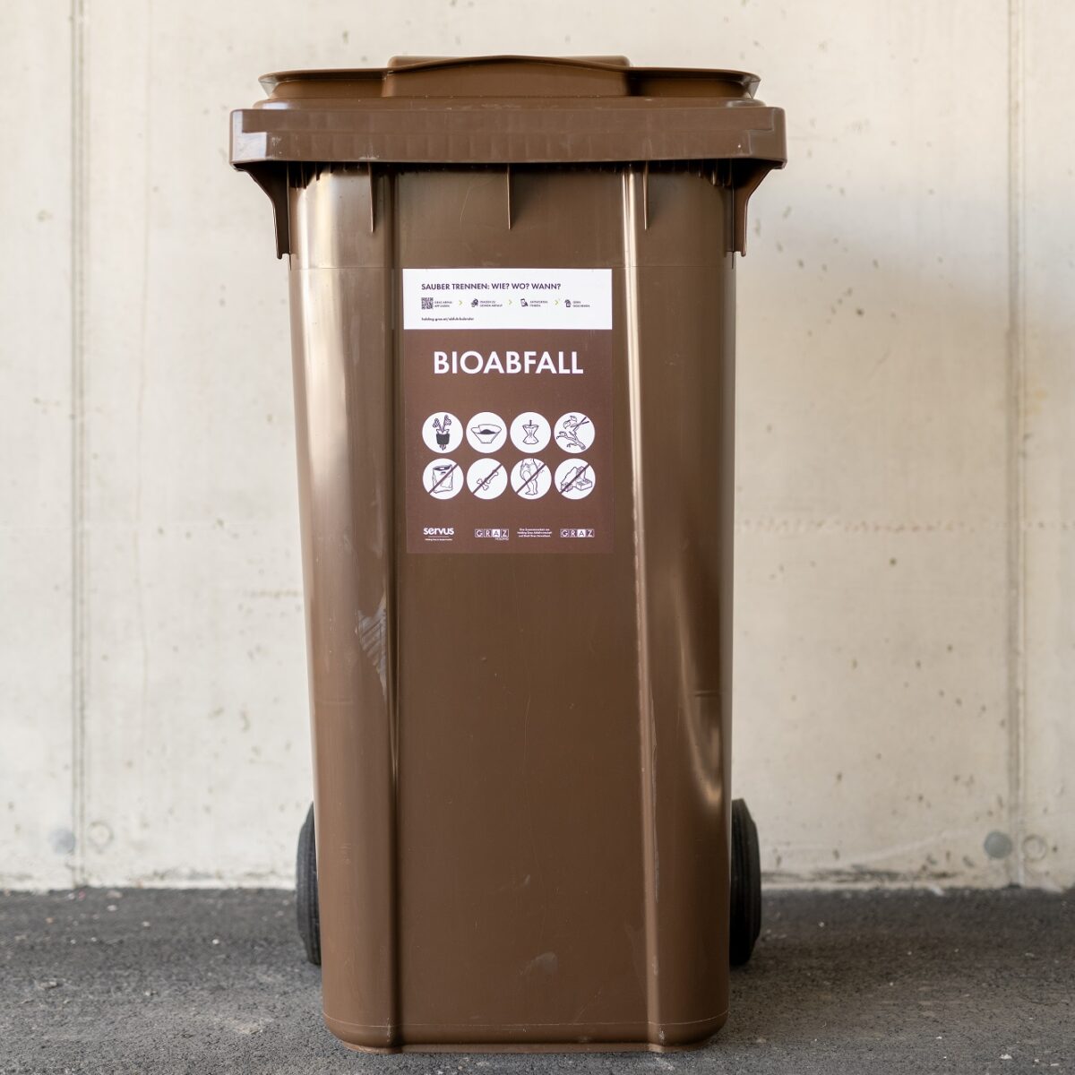 A brown, wheeled bin labeled "BIOABFALL" with a sticker showing what can and cannot be disposed of.