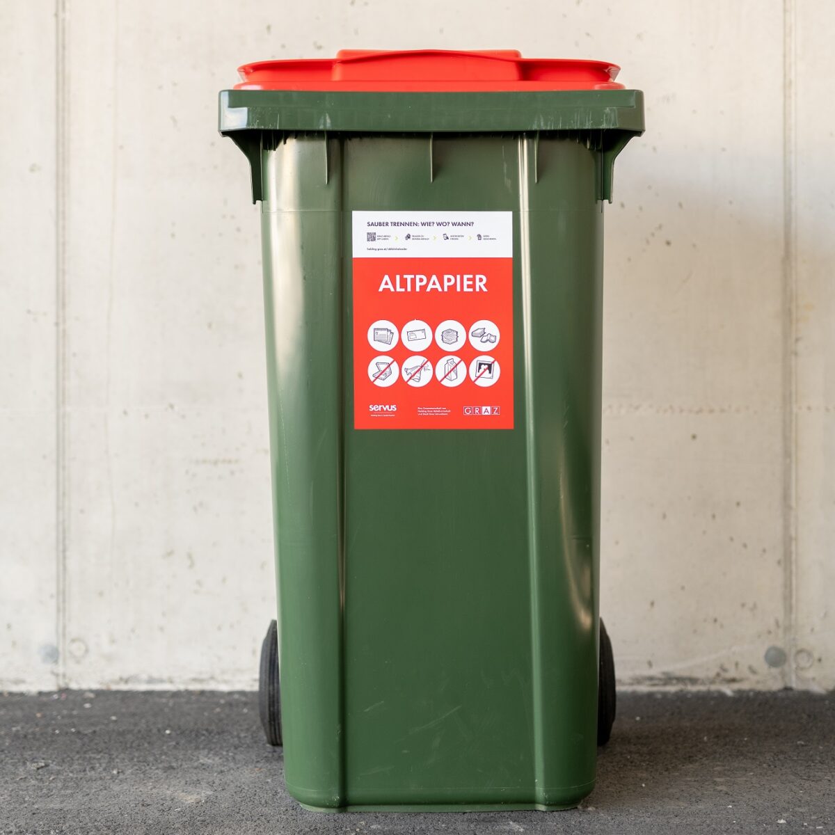 A green recycling bin with a red lid labeled "Altpapier" and several icons for permitted and forbidden items.