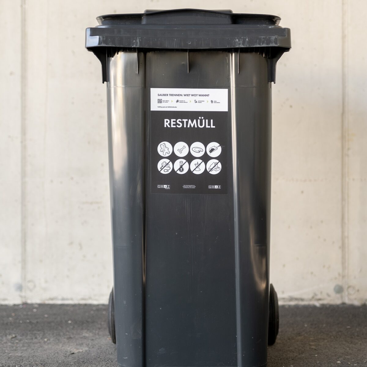 A gray trash bin labeled "Restmüll" with a sticker that says "Sauber trennen! Wie? Was? Wo? Wann?".