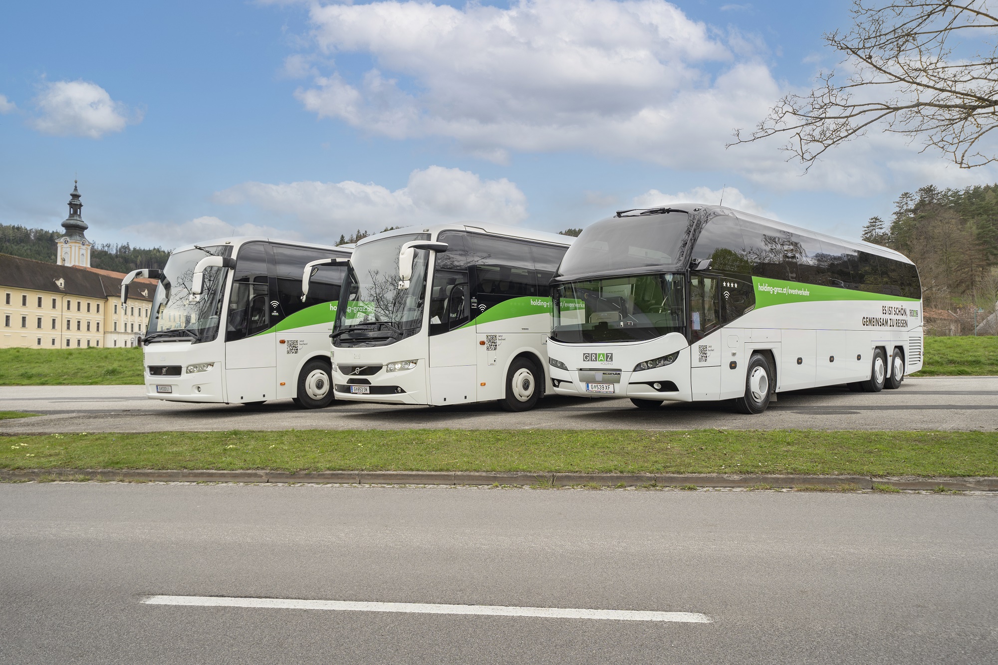 Three white buses with green accents parked in front of a building in Graz.