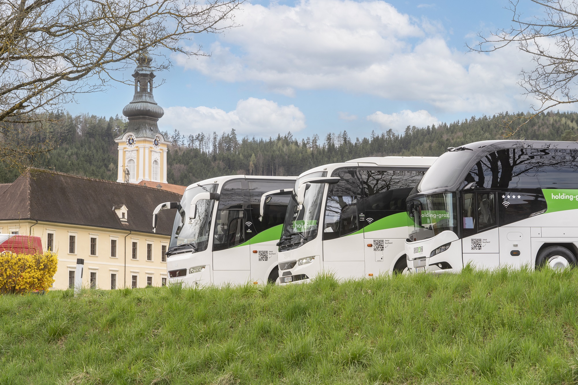Drei weiße Reisebusse der Graz Linien an sonnigem Tag vor einem Schloss.