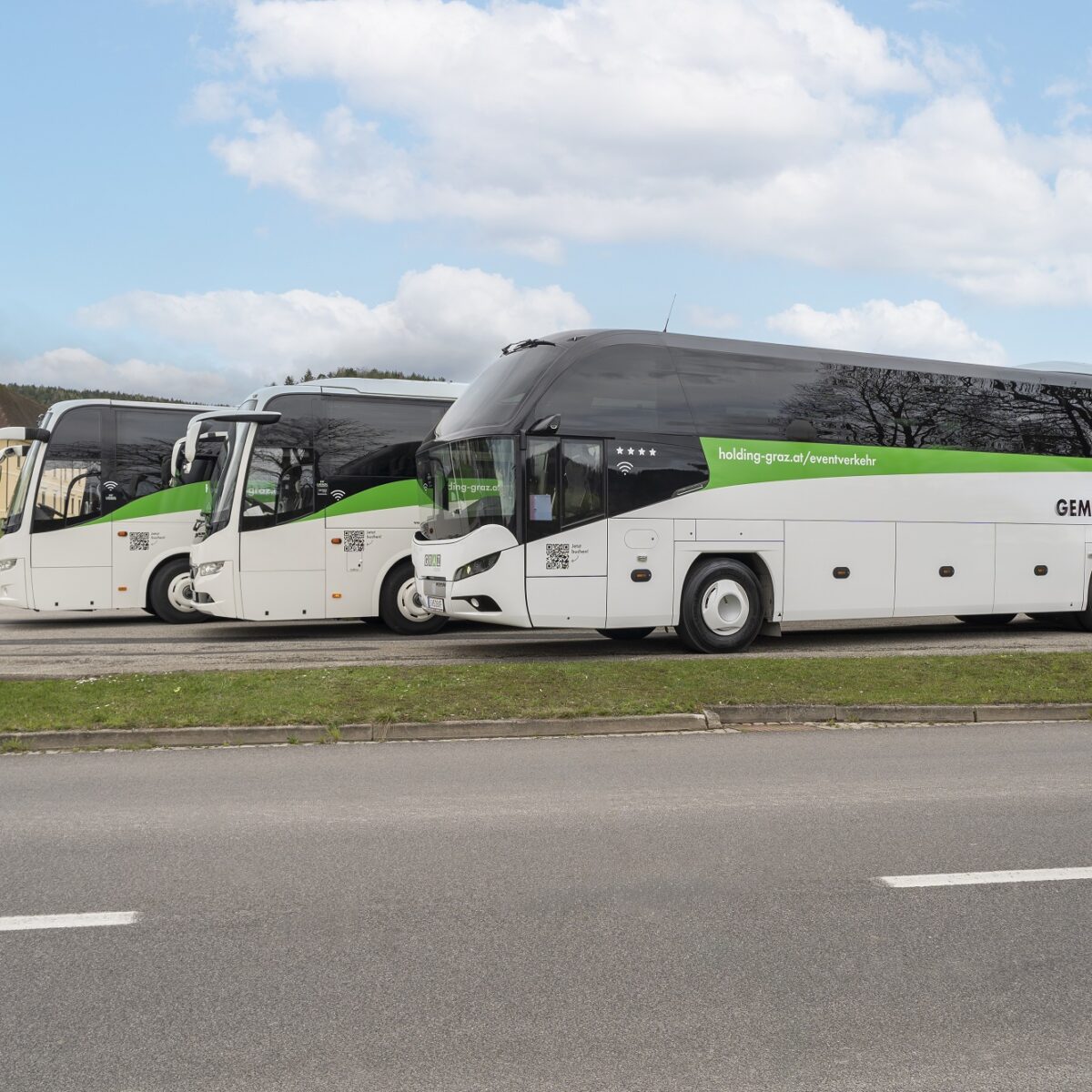 Three white Graz Linien coaches are parked in a lot, with the slogan "Es ist schön, gemeinsam zu reisen" visible on one.
