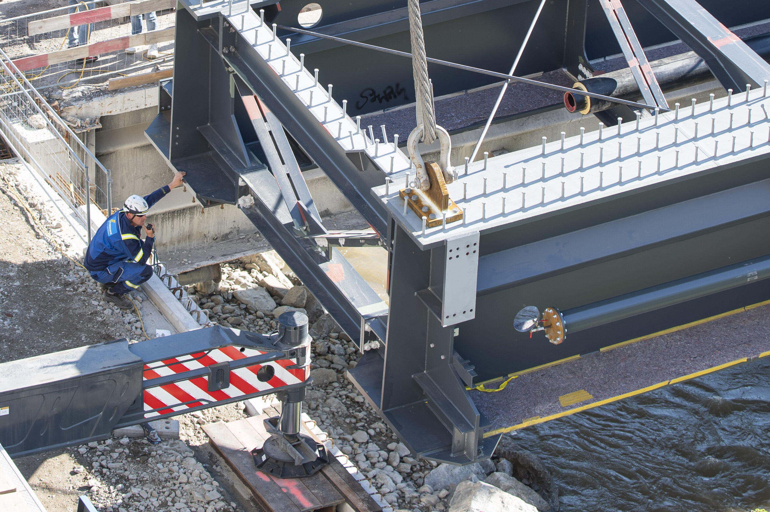 Ein Bauarbeiter überwacht die Installation einer neuen Brückenkonstruktion über einem Fluss.