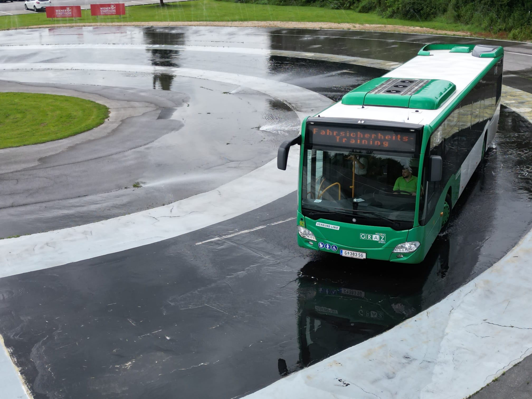 Ein grüner Bus der Graz Linien fährt auf einer nassen Fahrbahn im Fahrsicherheits-Training.