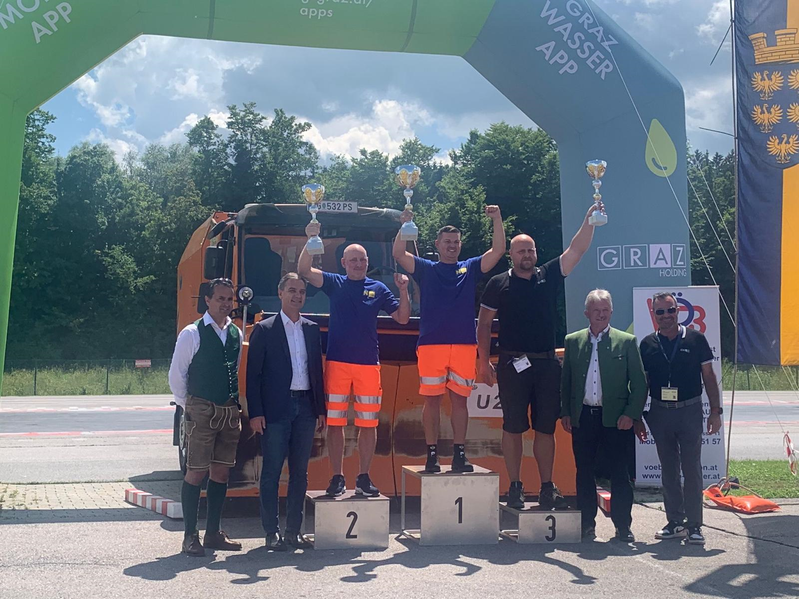 Siegerehrung der Schneepflug-Staatsmeisterschaften mit einem Schneepflug der Graz Holding im Hintergrund.
