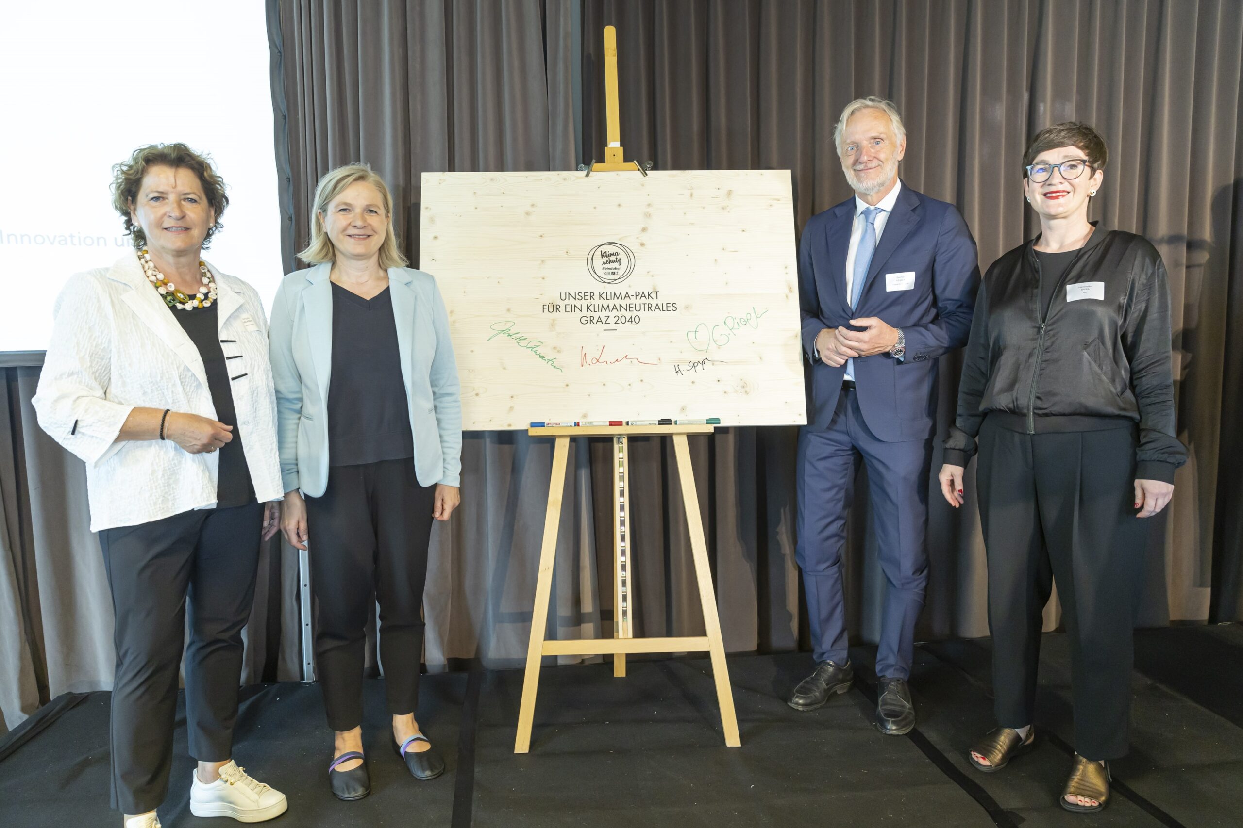 Vier Personen vor Schild mit Aufschrift „Unser Klima-Pakt für ein klimaneutrales Graz 2040“.