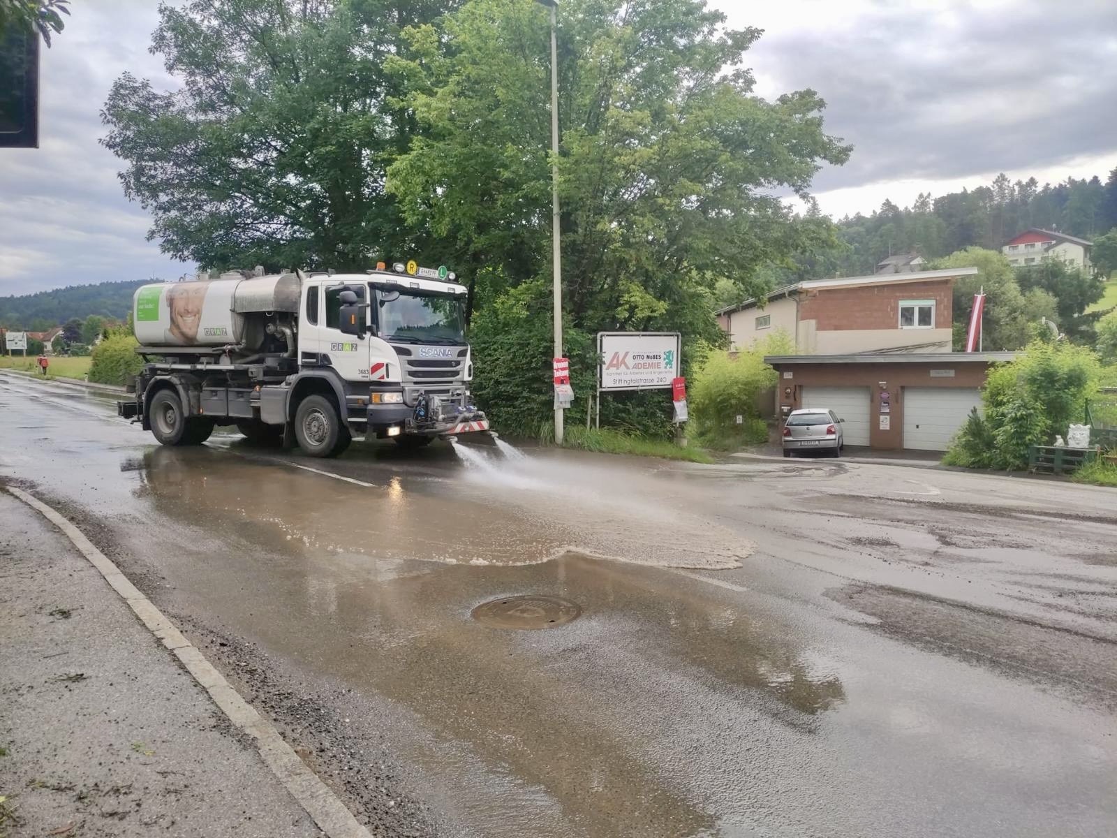 Ein weißer LKW mit Wasserwagen reinigt eine Straße nach einem Unwetter.