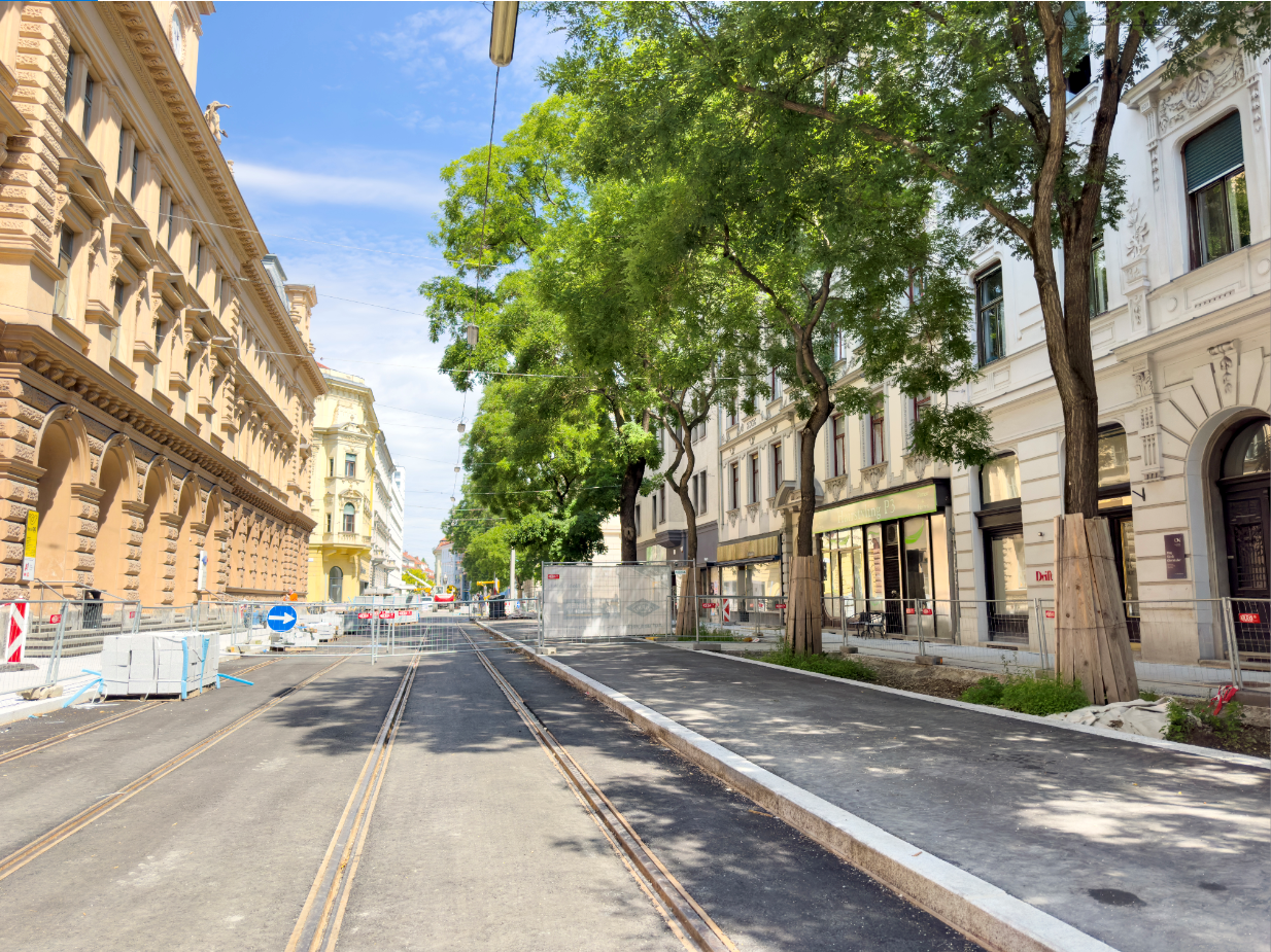 Straßenansicht der Neutorgasse in Graz mit Straßenbahn-Gleisen und Bäumen.