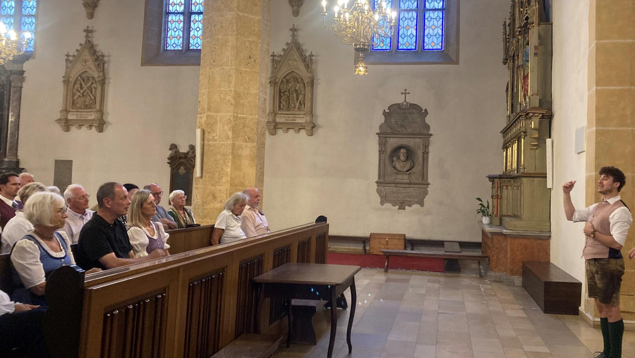 Ein Mann in Tracht führt eine Gruppe von Menschen durch eine Kirche.