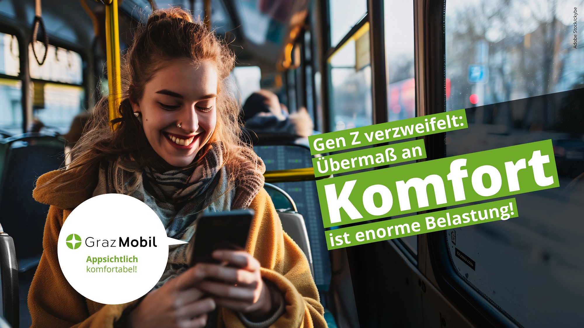 Eine junge Frau sitzt im Bus und schaut auf ihr Handy. "GrazMobil" ist auf Schild neben ihr zu sehen.