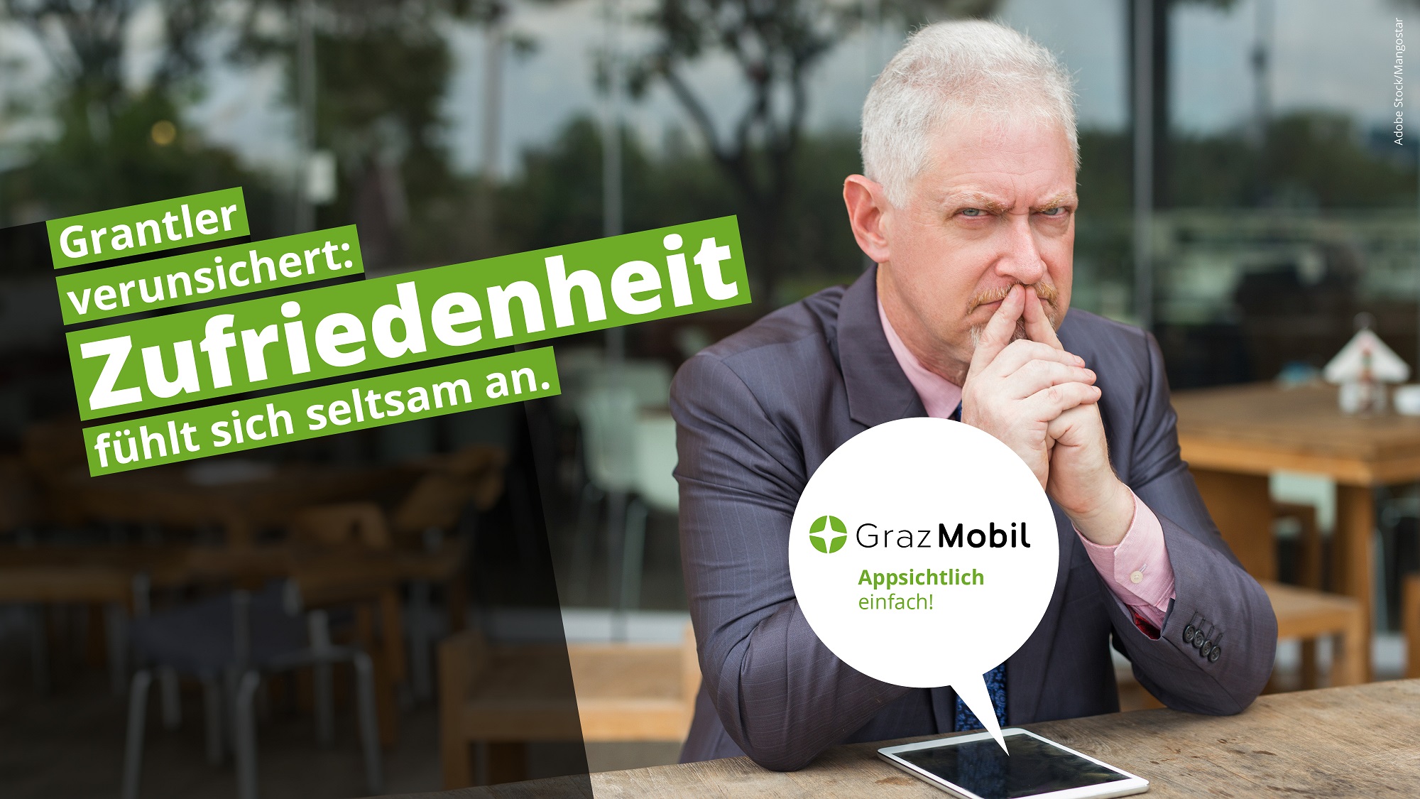 "GrazMobil"-Werbung: Mann sitzt an Tisch, Text: "Grantler verunsichert: Zufriedenheit fühlt sich seltsam an."