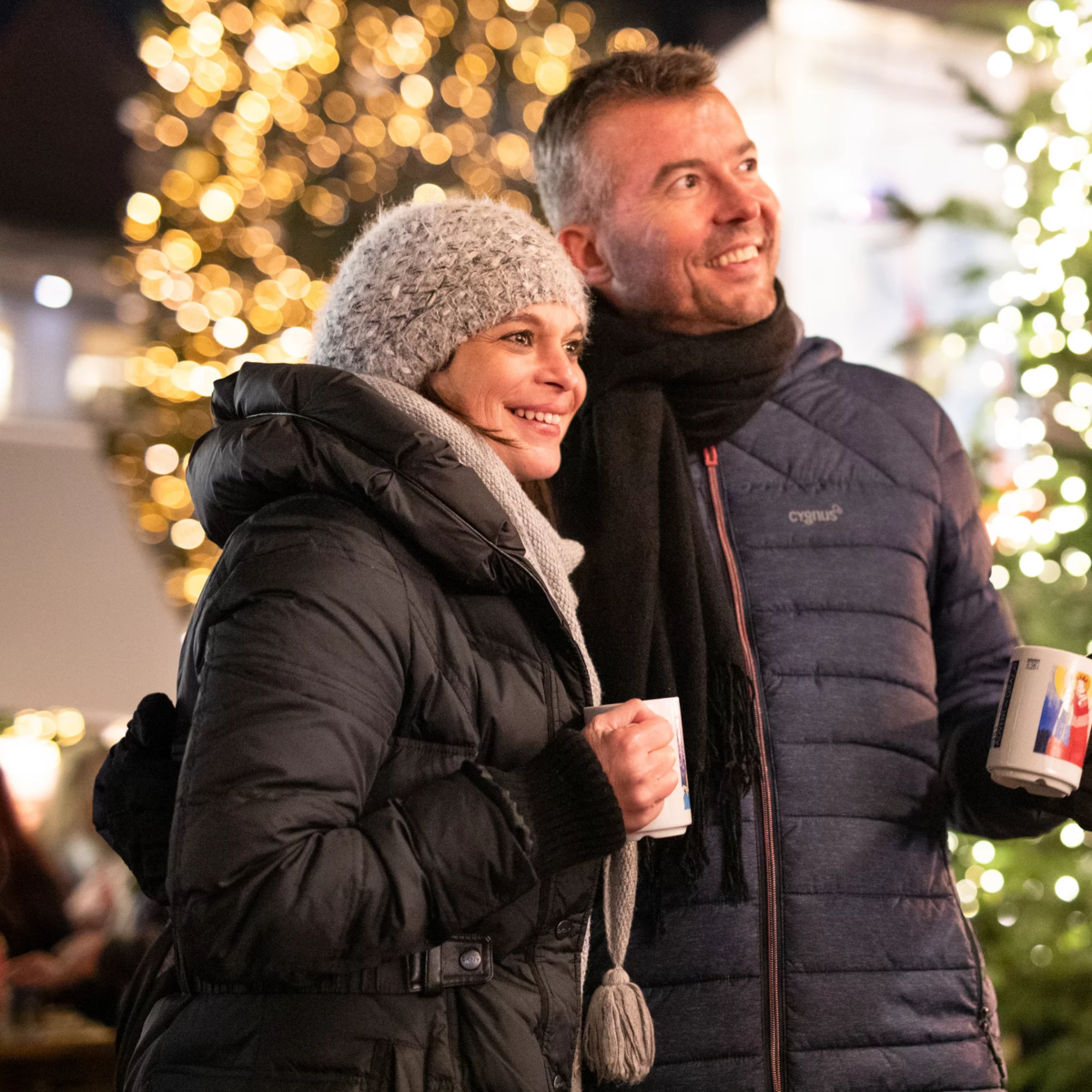 Ein Paar in Winterkleidung genießt Glühwein auf einem Weihnachtsmarkt.
