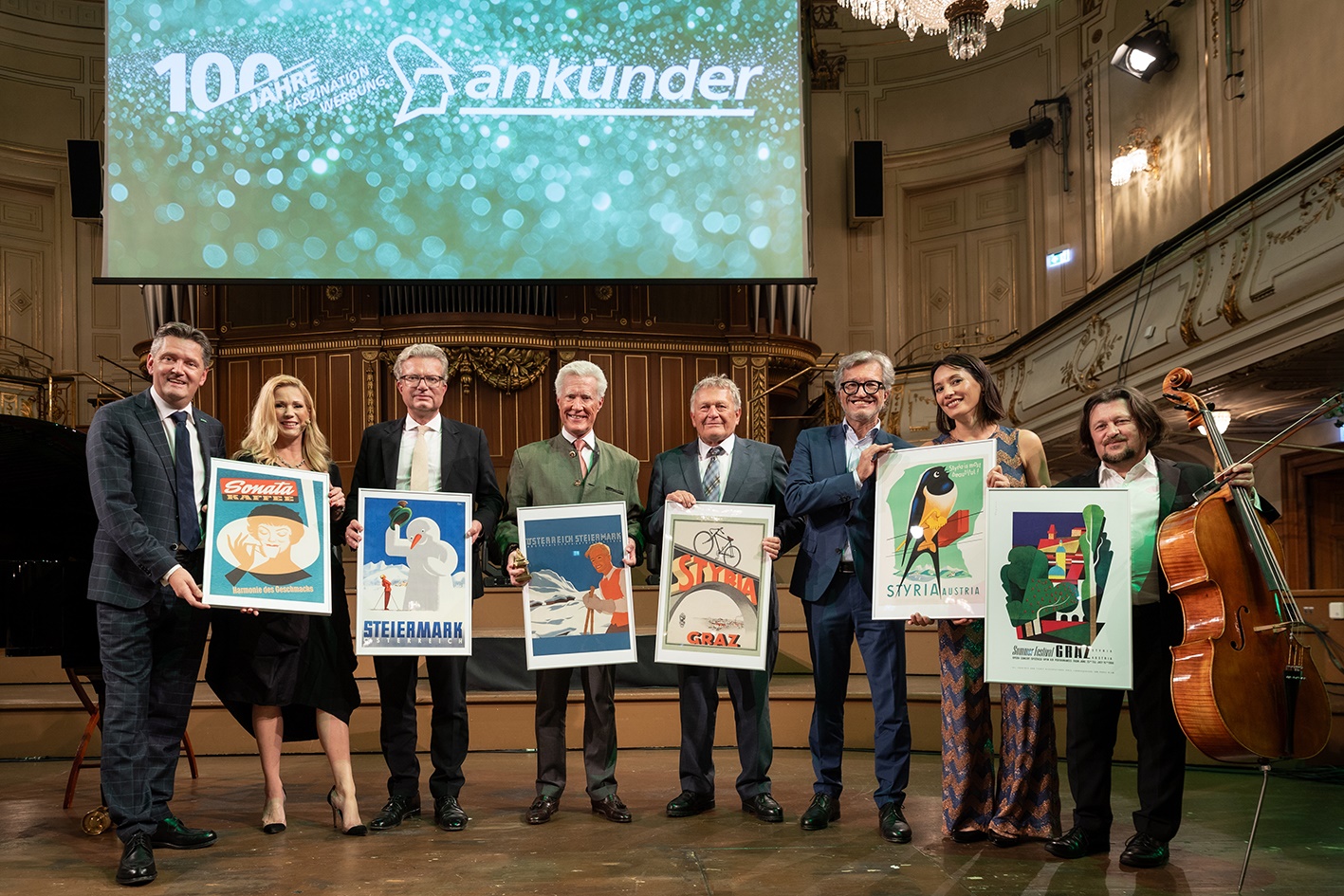 Eine Gruppe von acht Personen hält Plakate mit dem Schriftzug "Steiermark", "Styria" und "Graz".