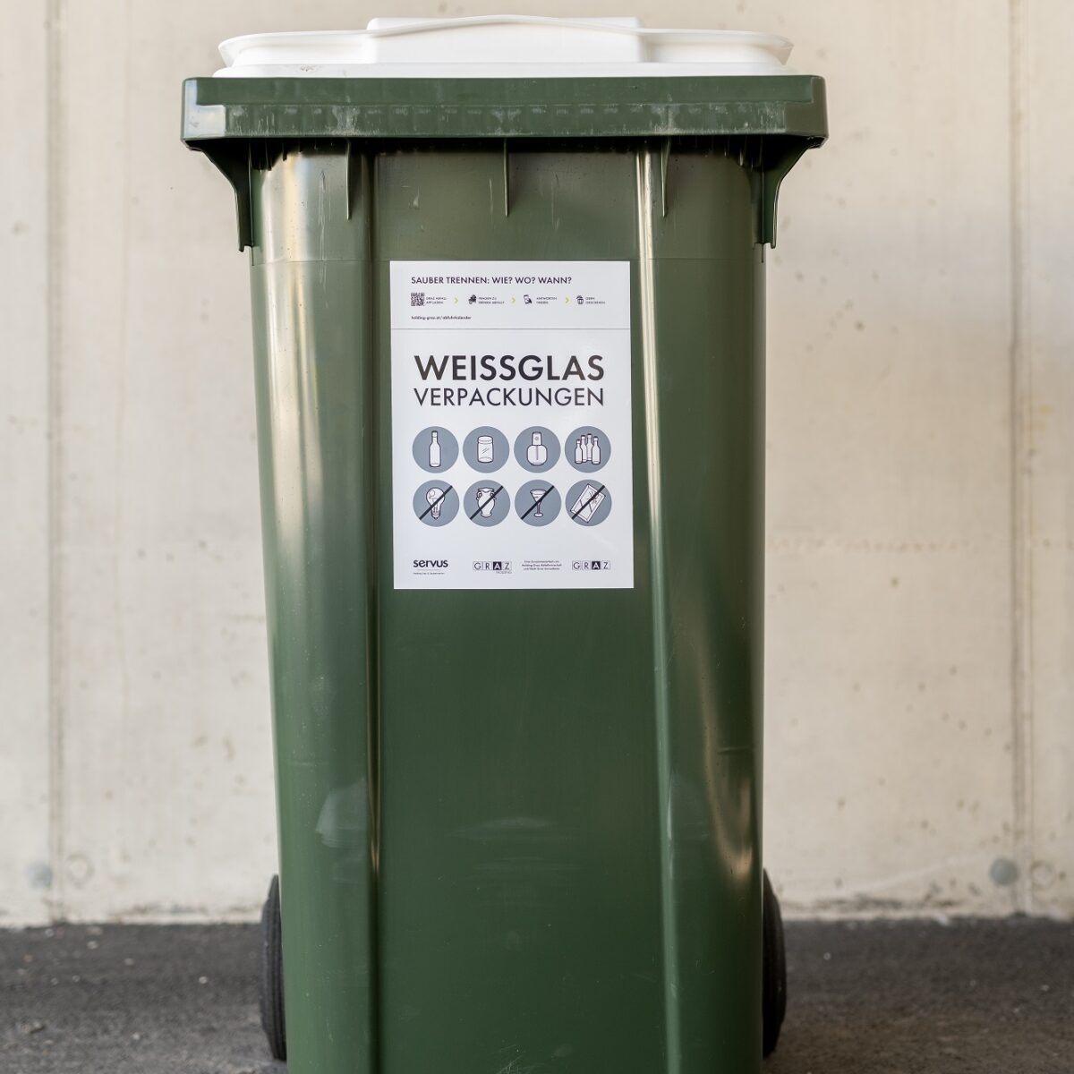 Green recycling bin with a white lid, labeled "Weissglas Verpackungen" (White Glass Packaging).
