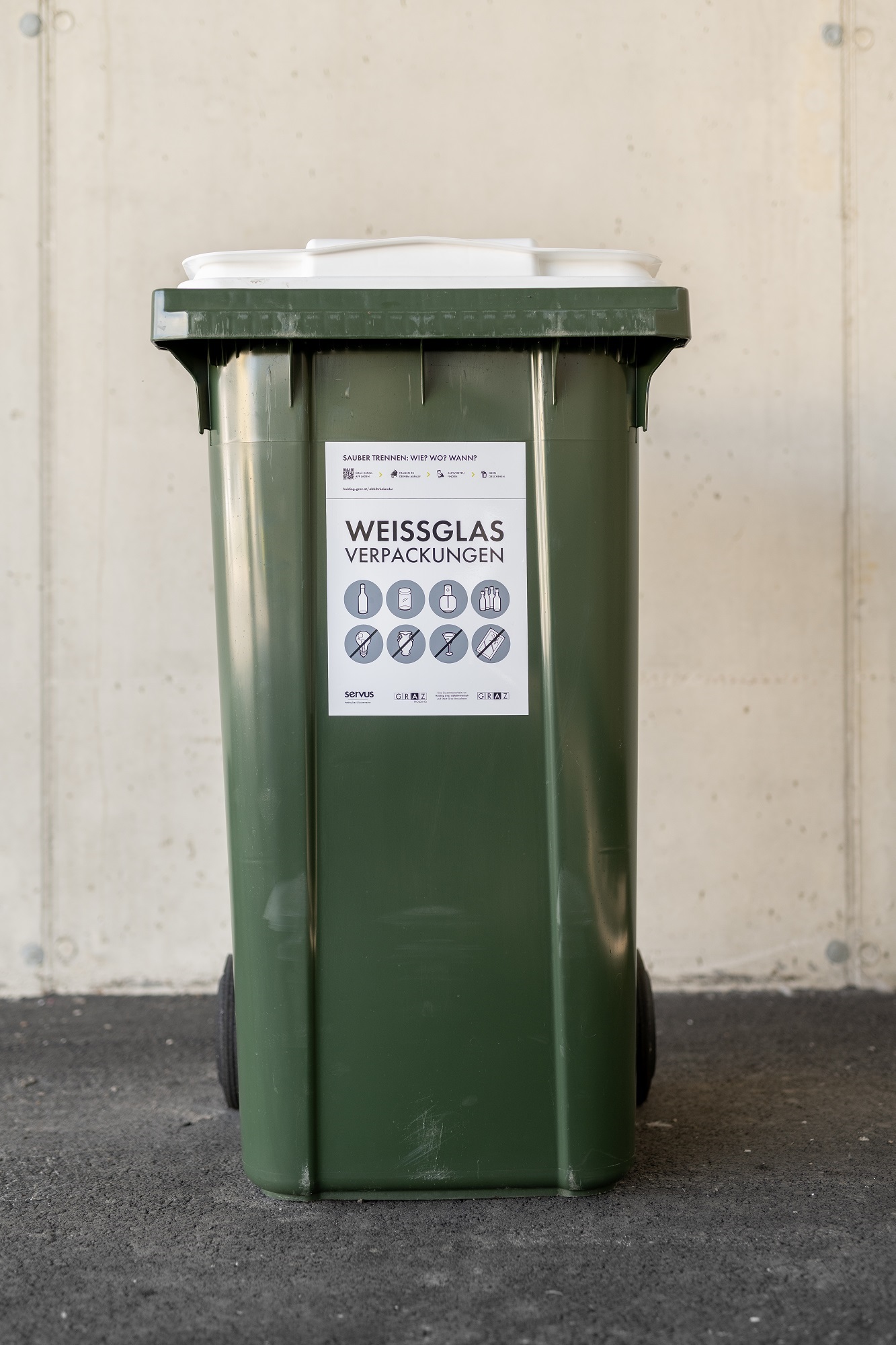 Green recycling bin with a white lid, labeled "Weissglas Verpackungen" (White Glass Packaging).