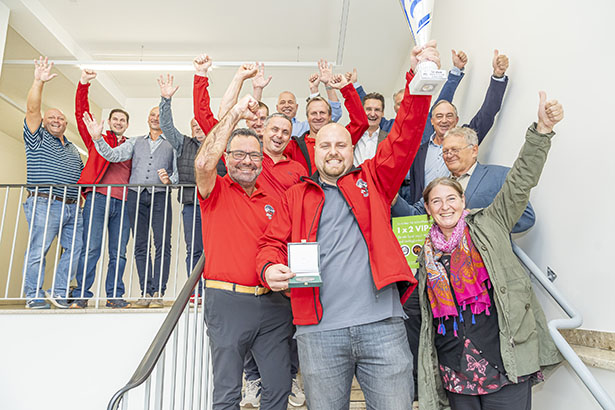 Gruppe von Menschen, darunter John Meierhofer, feiern mit erhobenen Armen und Pokal in der Hand.