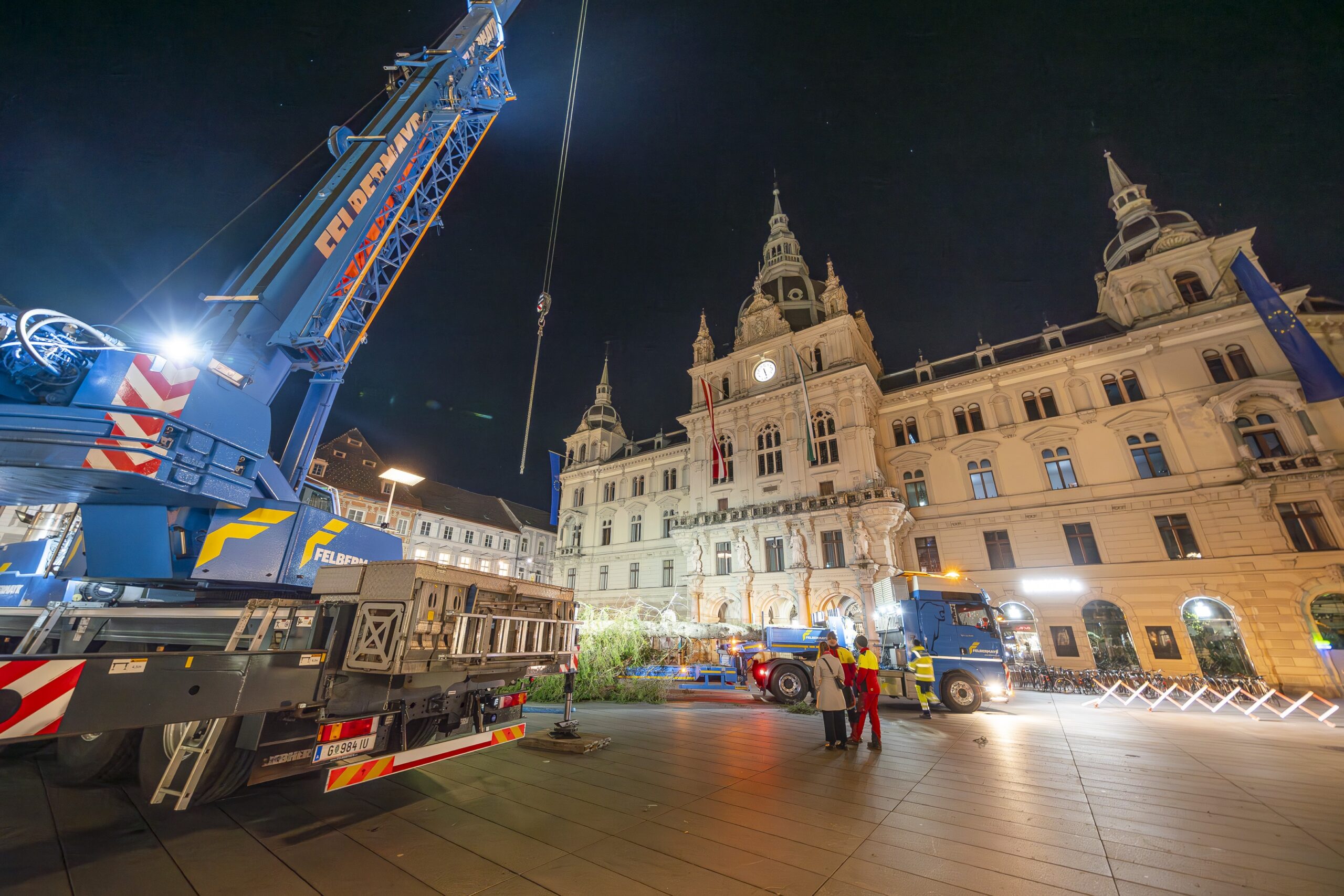 Aufstellung des Christbaumes am nächtlichen Hauptplatz: Baum hängt am Kran.