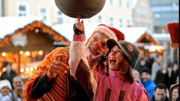 Clown Jako balanciert eine Kugel auf seinem Finger, während ein Kind begeistert zuschaut.