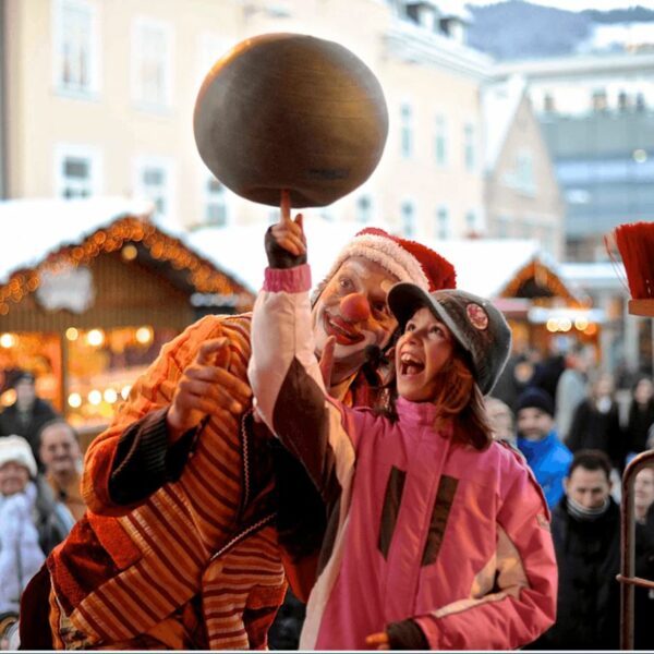 Clown Jako balanciert eine Kugel auf seinem Finger, während ein Kind begeistert zuschaut.