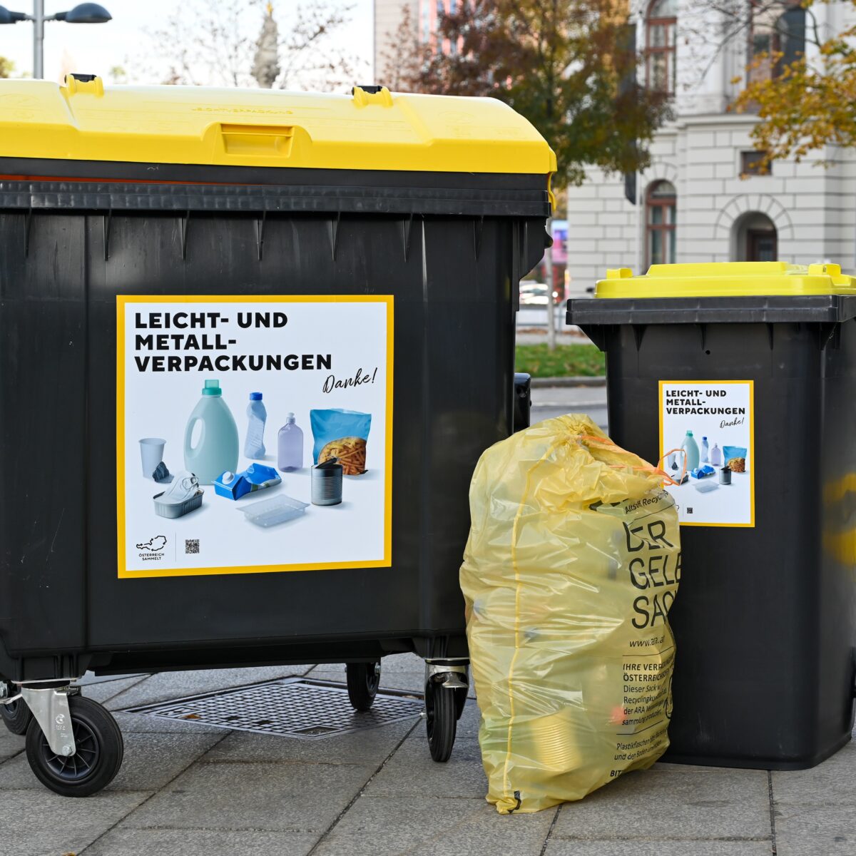 Two black recycling bins with yellow lids and yellow garbage bag labeled "Leicht- und Metall-Verpackungen"