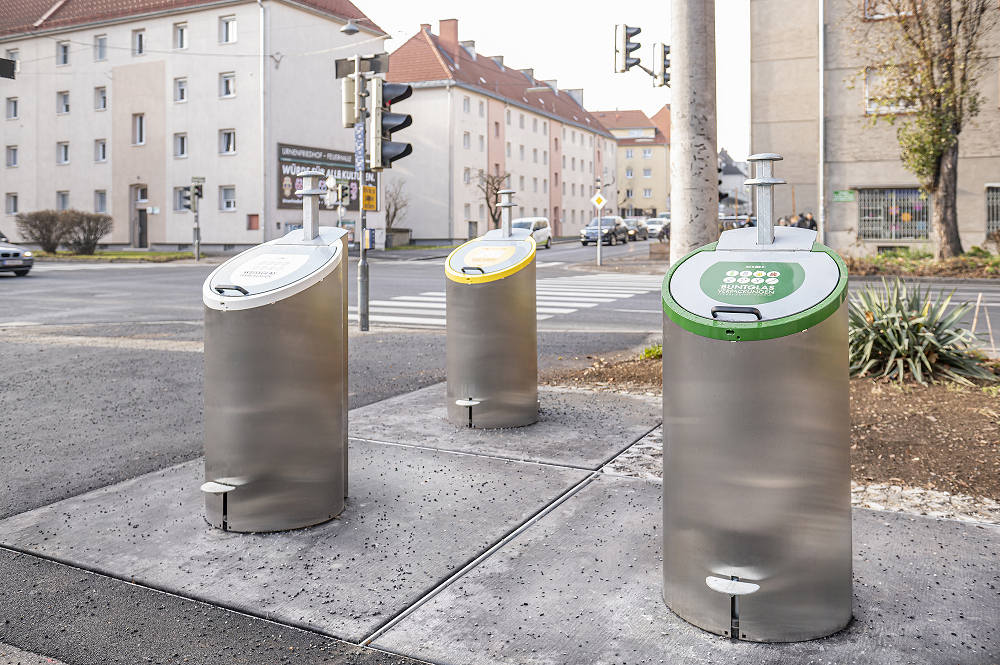 Drei unterirdische Müllcontainer in Graz. Grüner Container ist beschriftet mit „BUNTGLAS“.
