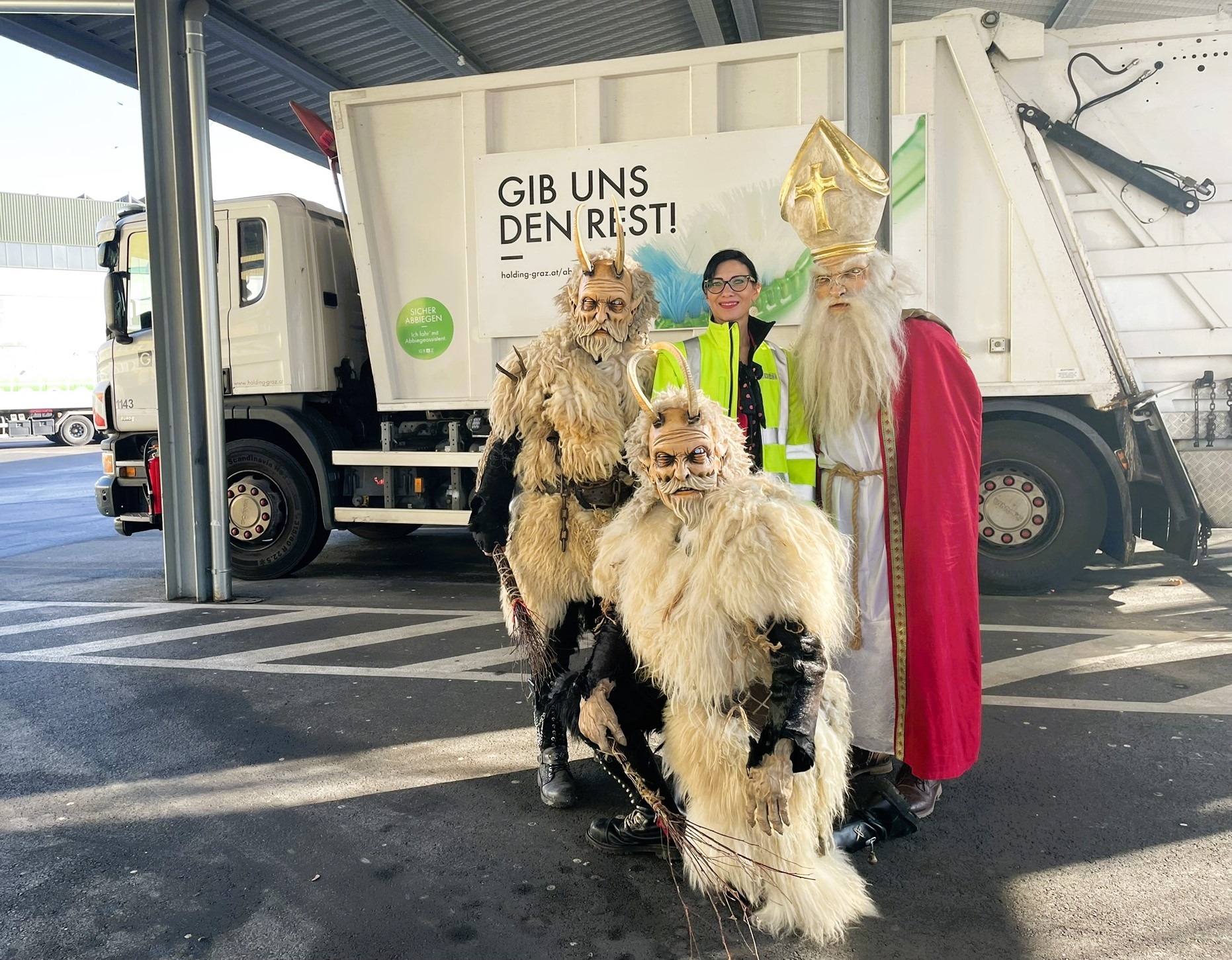 Nikolaus und Krampusse mit Alice Loidl vor einem Müllwagen mit dem Spruch "Gib uns den Rest!"