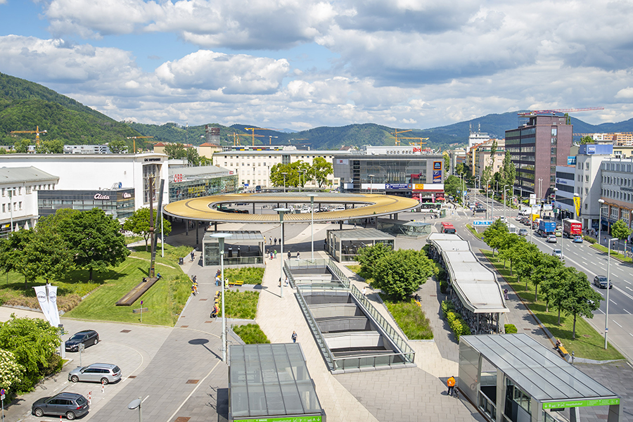 Der Hauptbahnhof Graz mit einem runden Dach und Grünflächen von schräg oben aufgenommen.