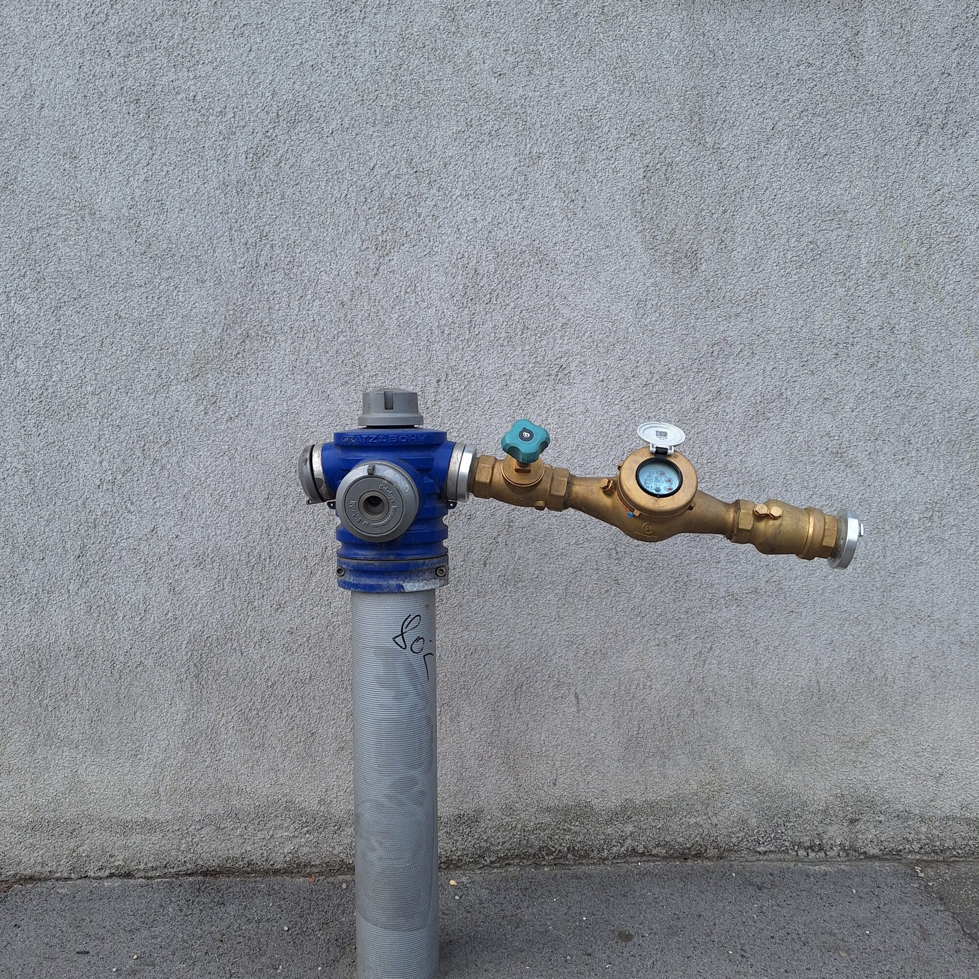 A blue hydrant stands in front of a gray wall.
