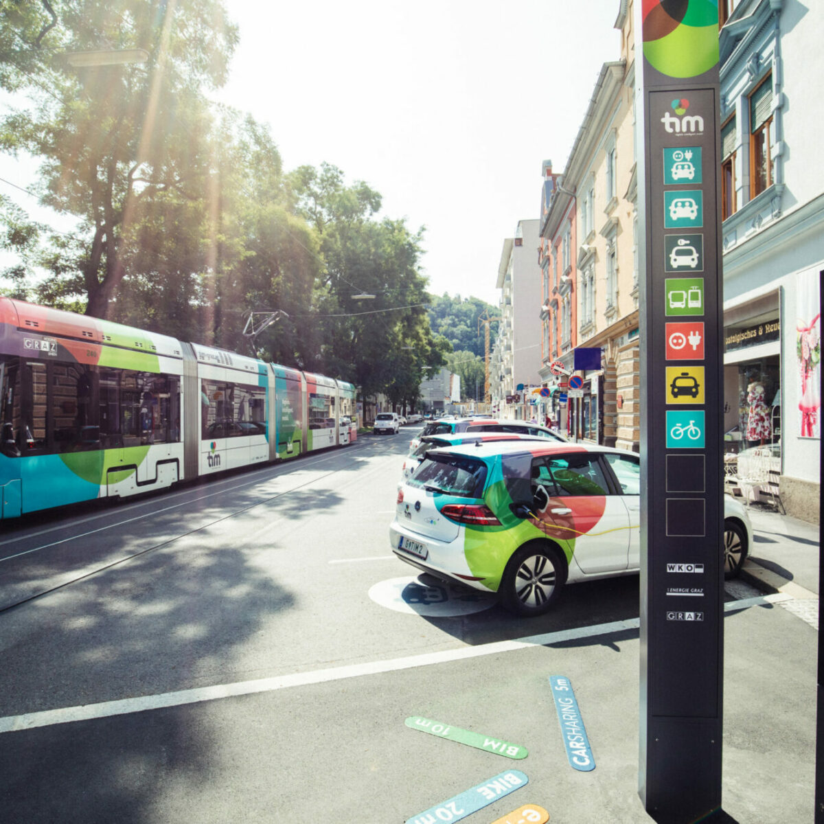tim-Knotenpunkt Hasnerplatz mit Pylon, E-Golf-Fahrzeugen und vorbeifahrender tim-Variobahn