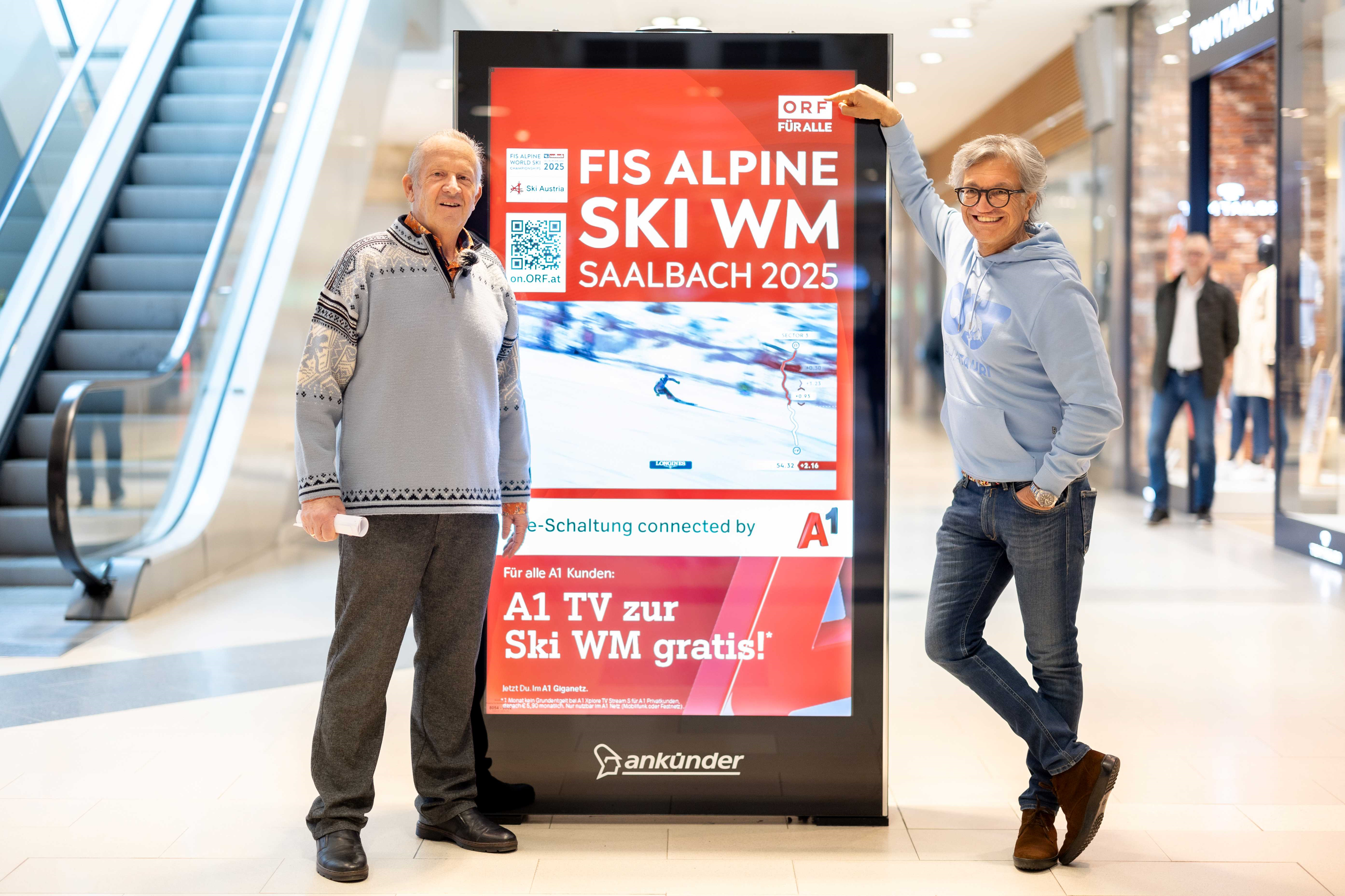 Zwei Männer vor einem Bildschirm mit der Aufschrift "FIS Alpine Ski WM Saalbach 2025".