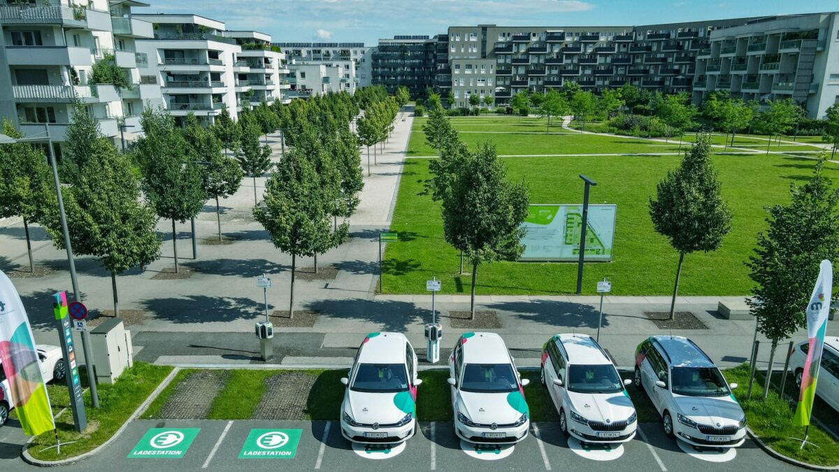 Vier tim-Fahrzeuge stehen am tim-Linz Standort Grüne Mitte, dahinter Wiese und Siedlung