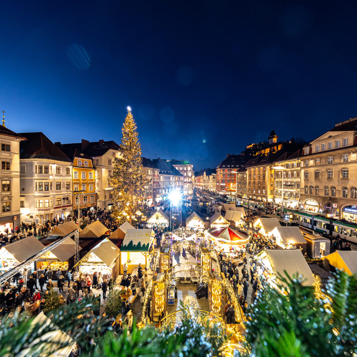 Blick von oben auf Weihnachtsmarkt in Graz mit Weihnachtsbaum und vielen Buden.