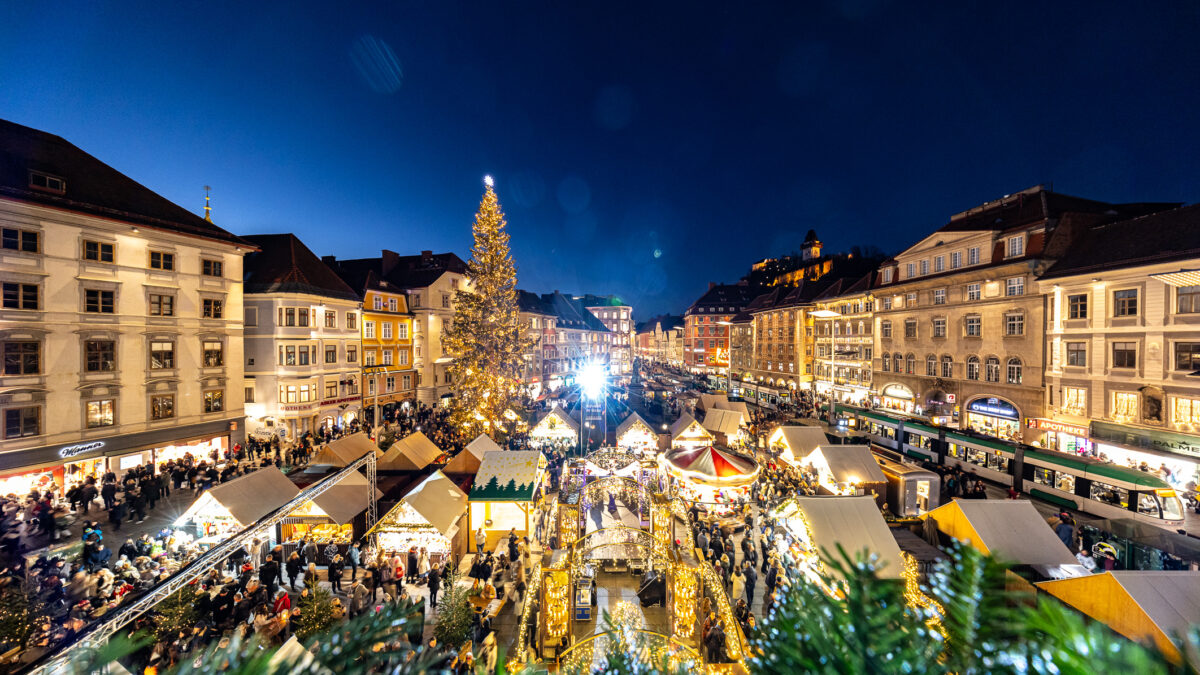 Blick von oben auf Weihnachtsmarkt in Graz mit Weihnachtsbaum und vielen Buden.