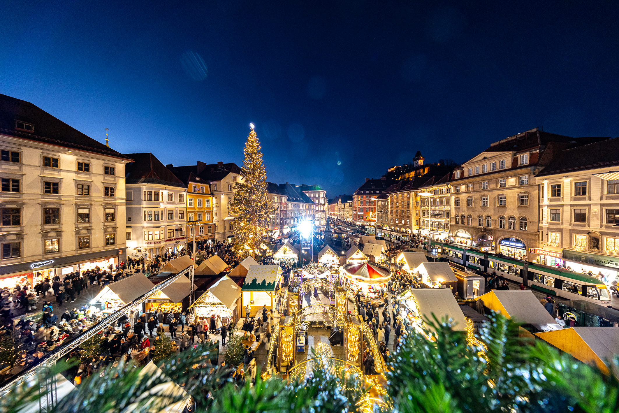 Blick von oben auf Weihnachtsmarkt in Graz mit Weihnachtsbaum und vielen Buden.