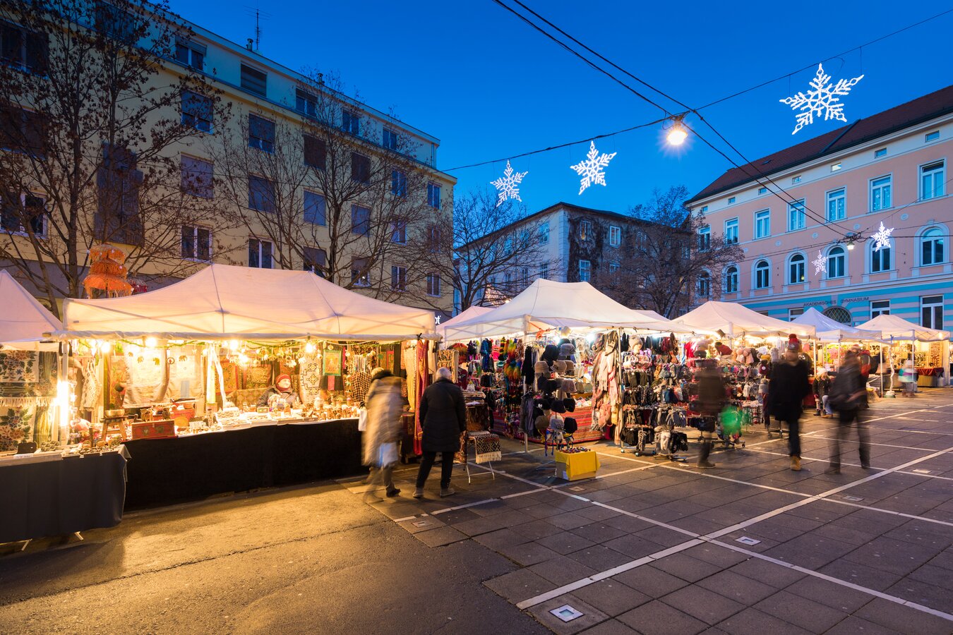 A night scene of a Graz Christmas market with snow flake lights.