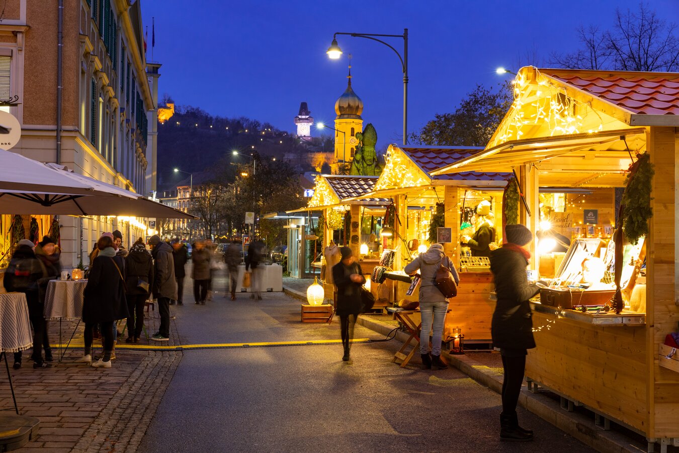 Graz market at night. People stroll past lit stalls.