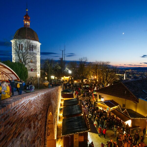 Blick auf den Grazer Schlossberg mit Weihnachtsmarkt bei Nacht.