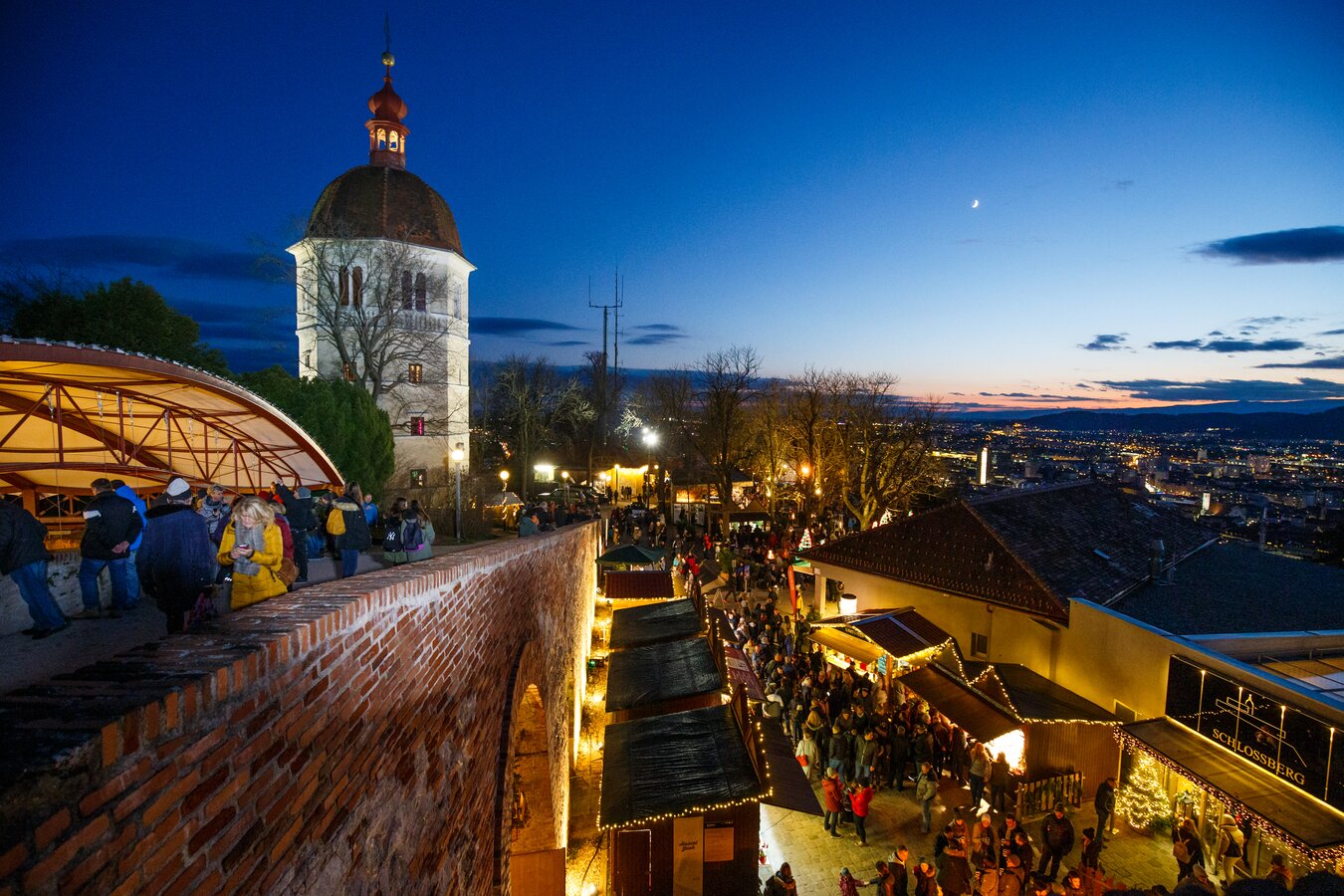 Blick auf den Grazer Schlossberg mit Weihnachtsmarkt bei Nacht.