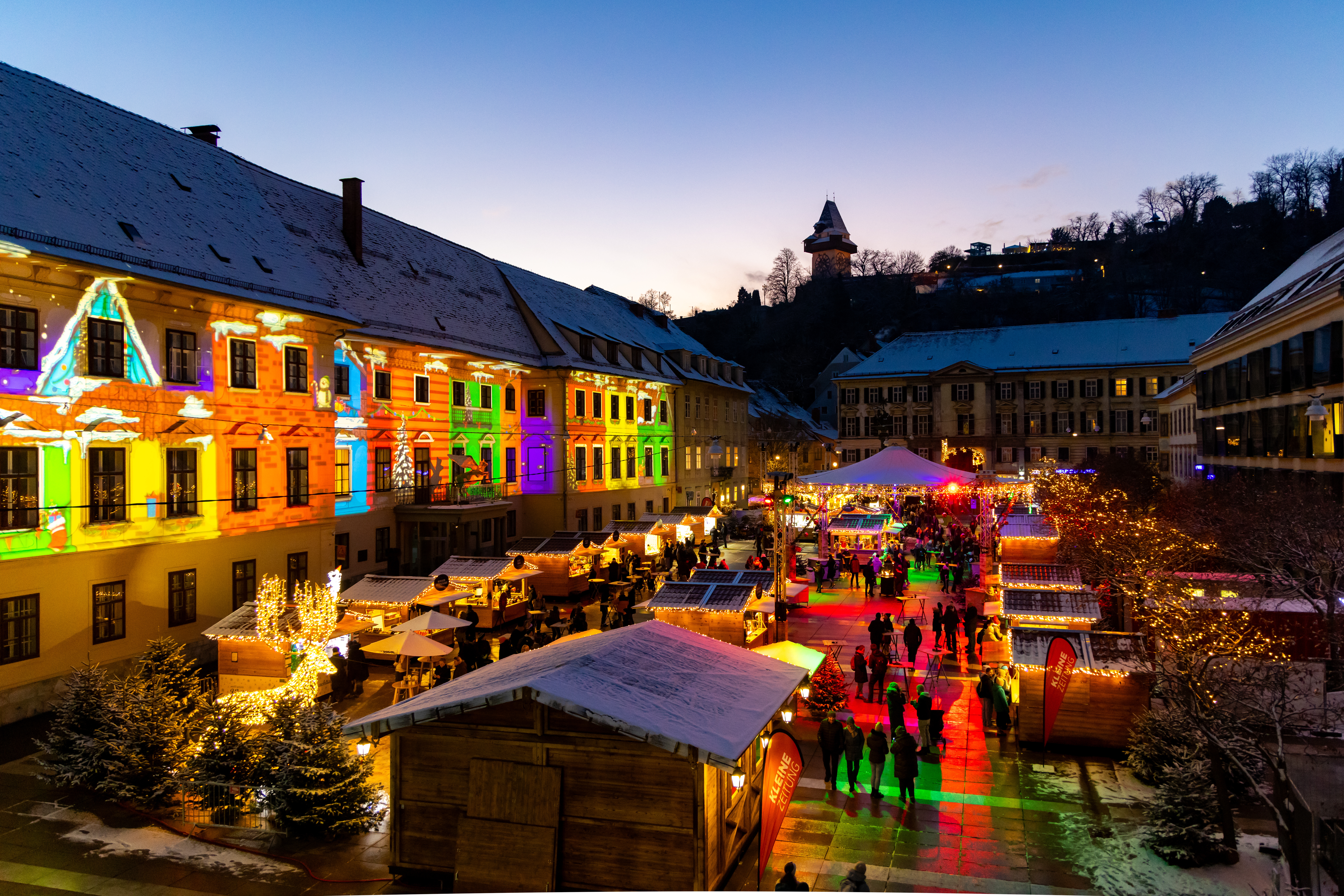 Graz Hauptplatz Christmas market at dusk with colorful lights.