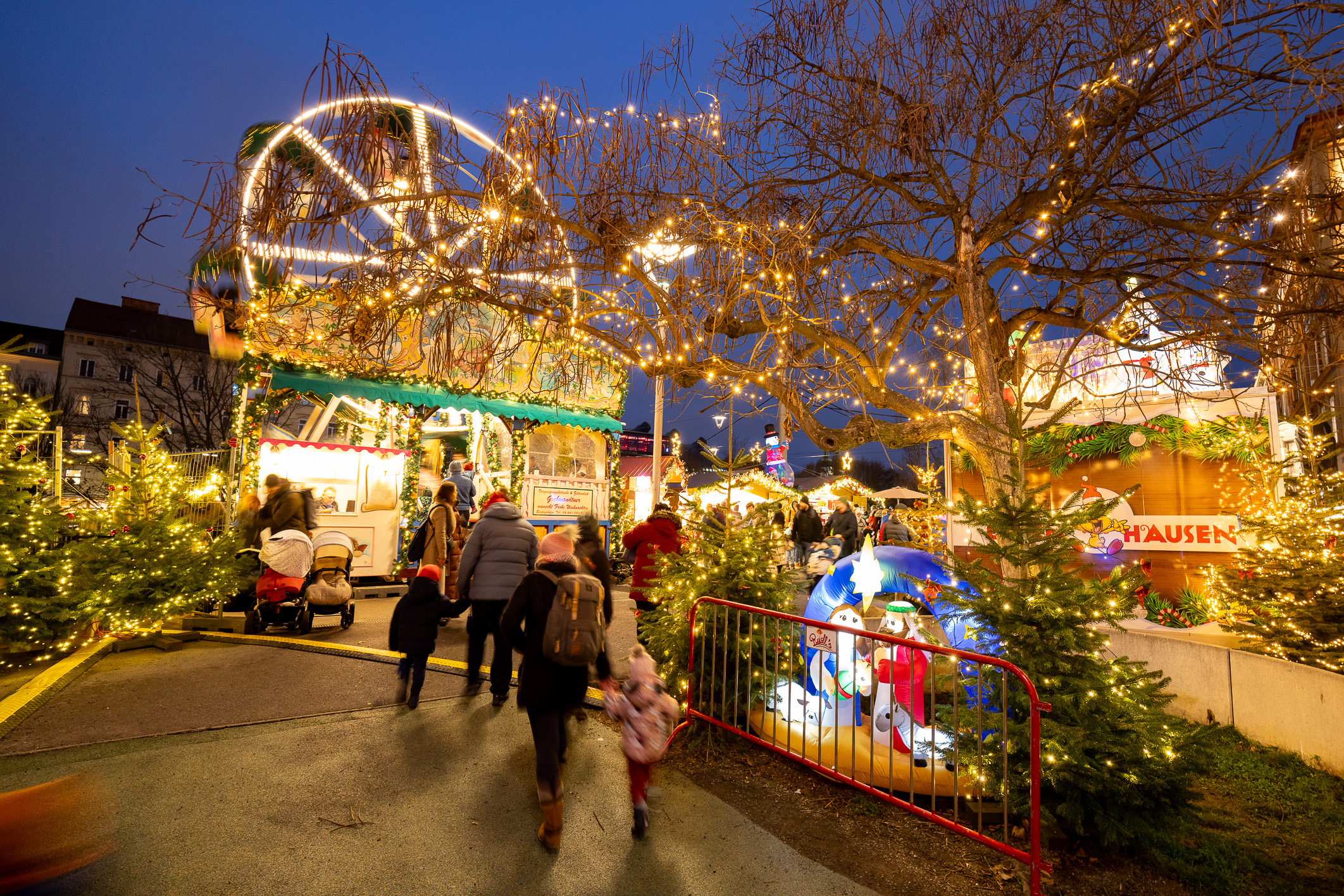 Graz Christmas market with Ferris wheel, lights, and Nativity scene.