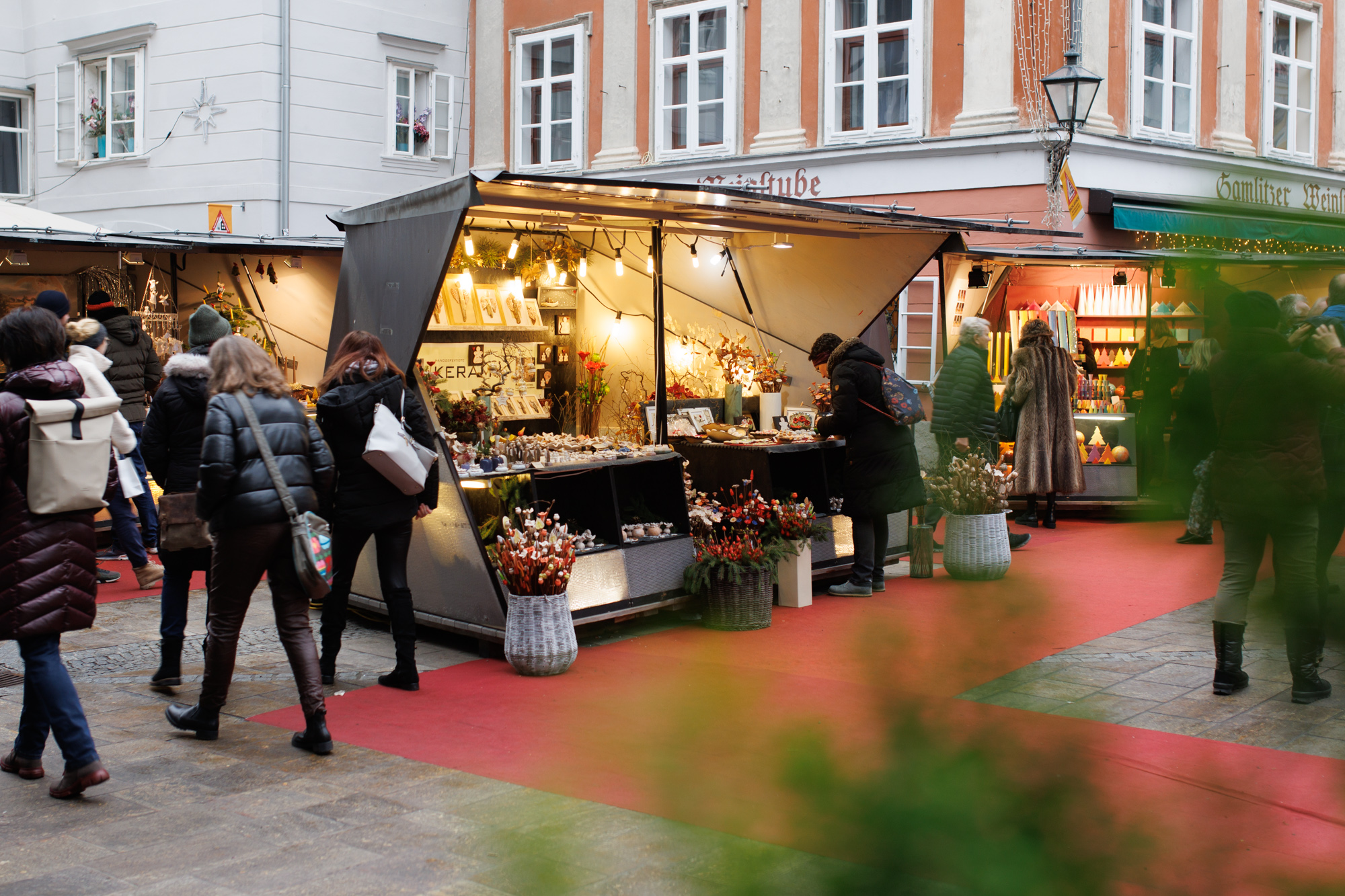 Graz market scene with shoppers browsing stalls. "Keramik" sign visible.