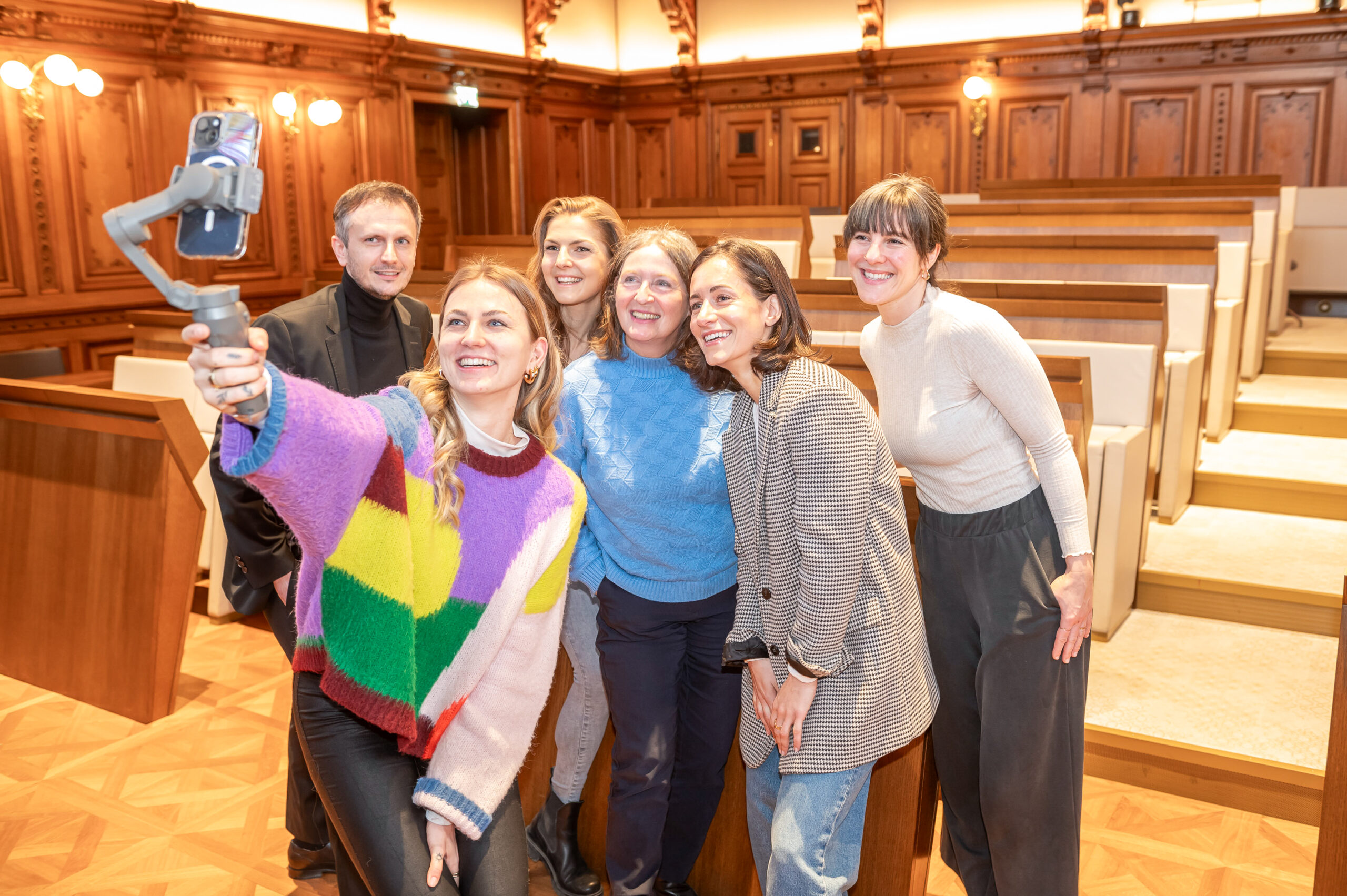 Sechs Personen posieren für ein Selfie in einem holzvertäfelten Raum.