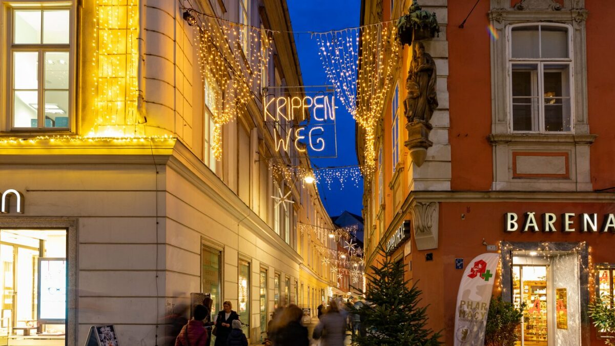 Blick in den Krippenweg in Graz mit Weihnachtsbeleuchtung und Passanten.