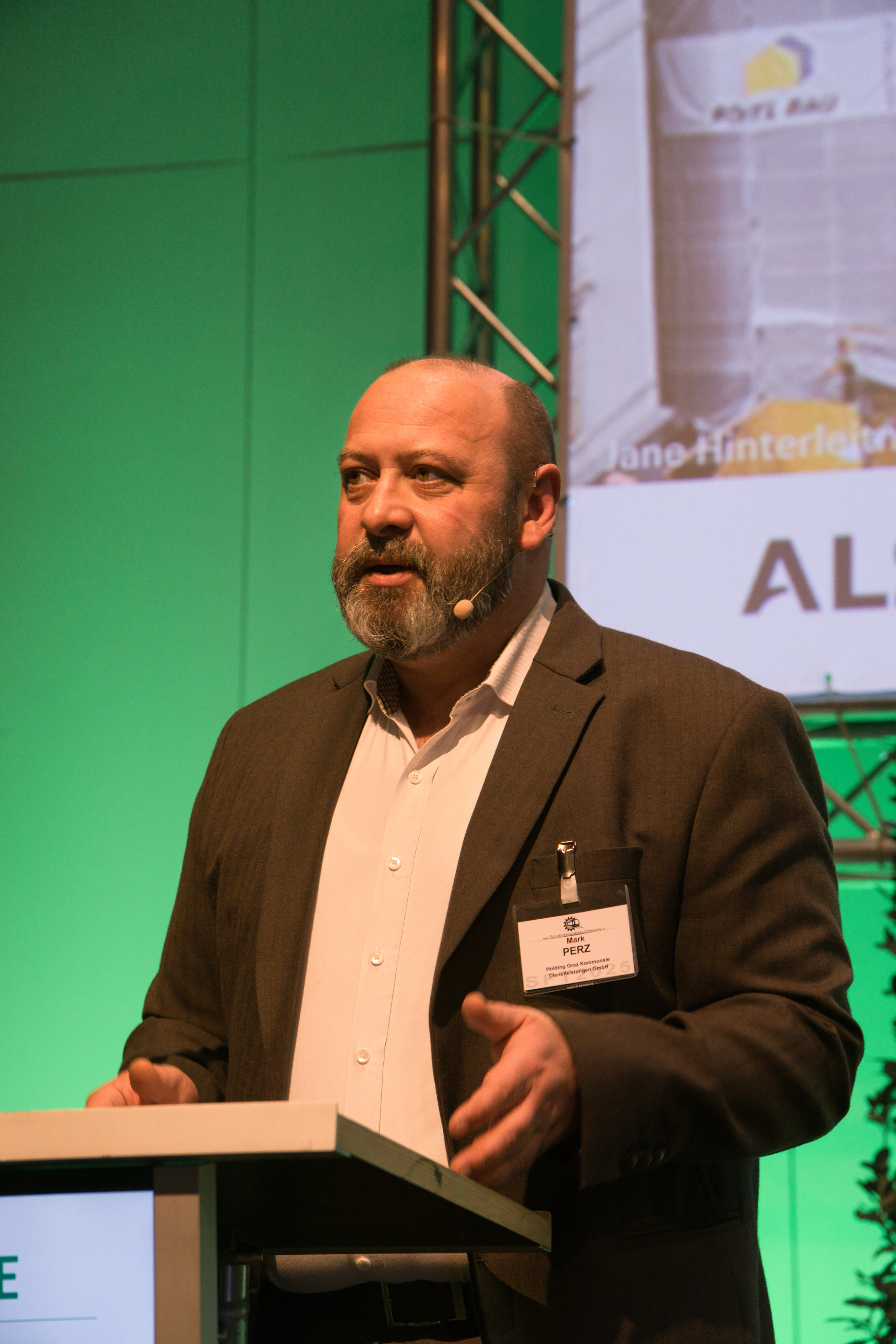 Mark Perz spricht am Rednerpult vor grünem Hintergrund.