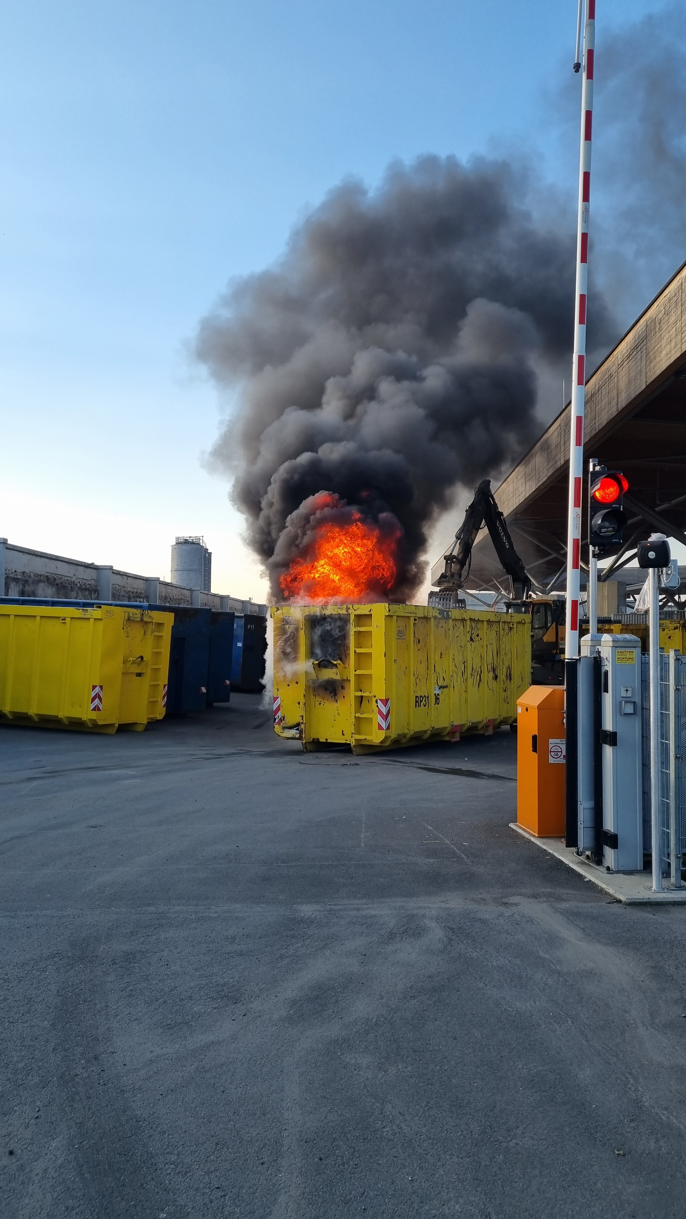 Gelber Container in Graz steht in Flammen, dichter Rauch. Bagger im Hintergrund.