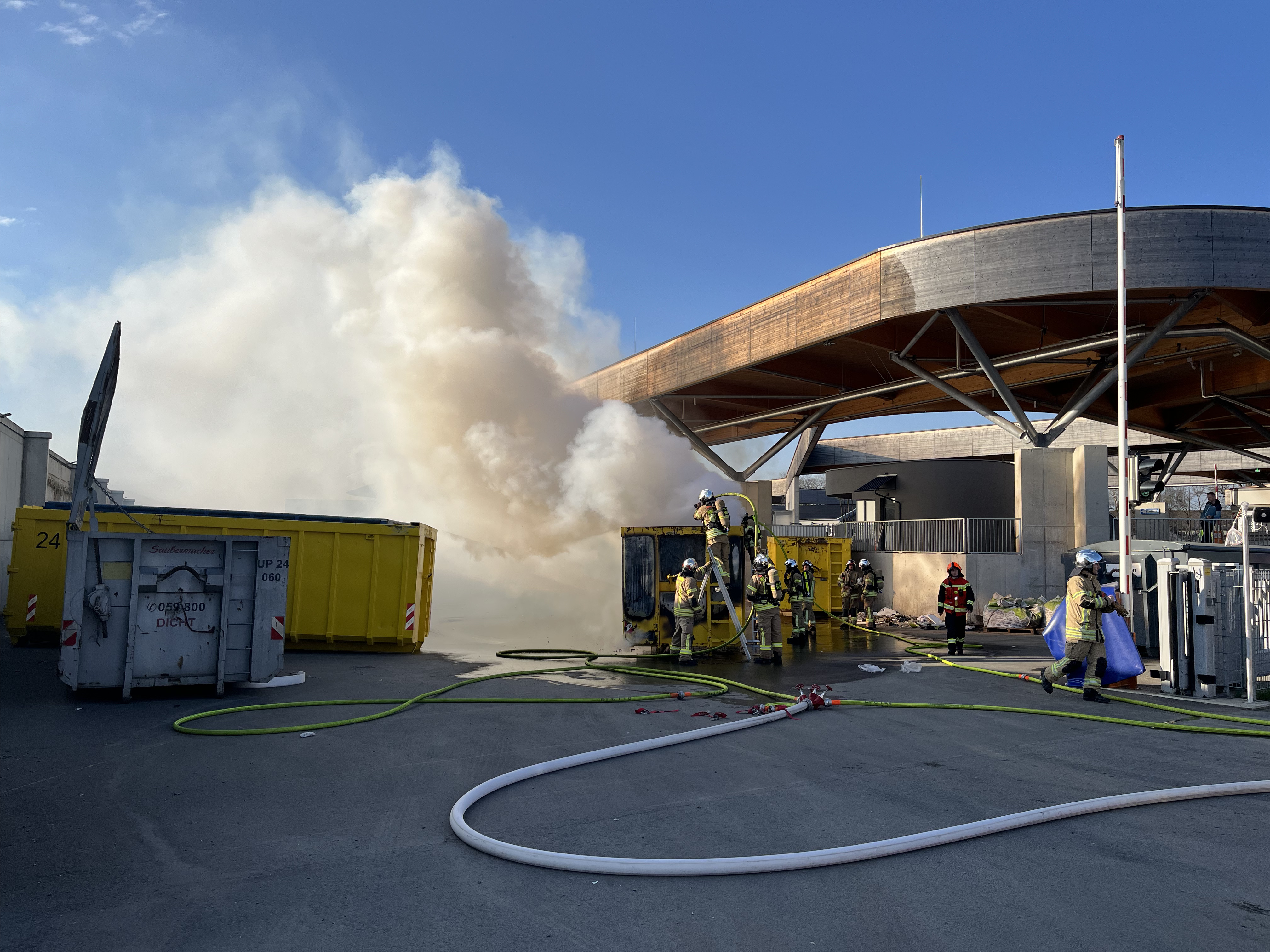 Gelbe Müllcontainer in Graz brennen, Feuerwehrleute löschen den Brand.