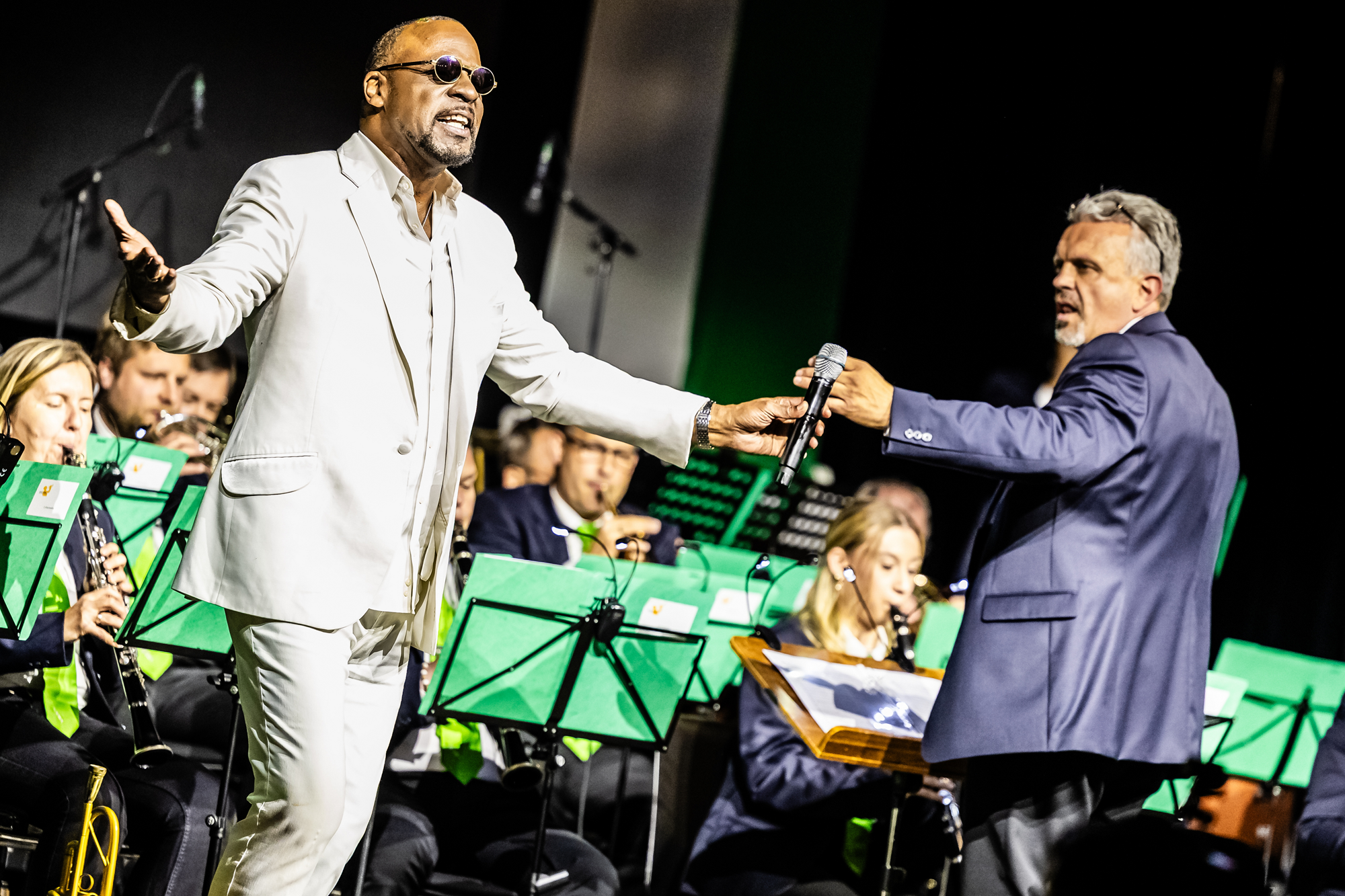 Ein Mann im weißen Anzug singt mit Orchester in Graz, Mikrofonübergabe.