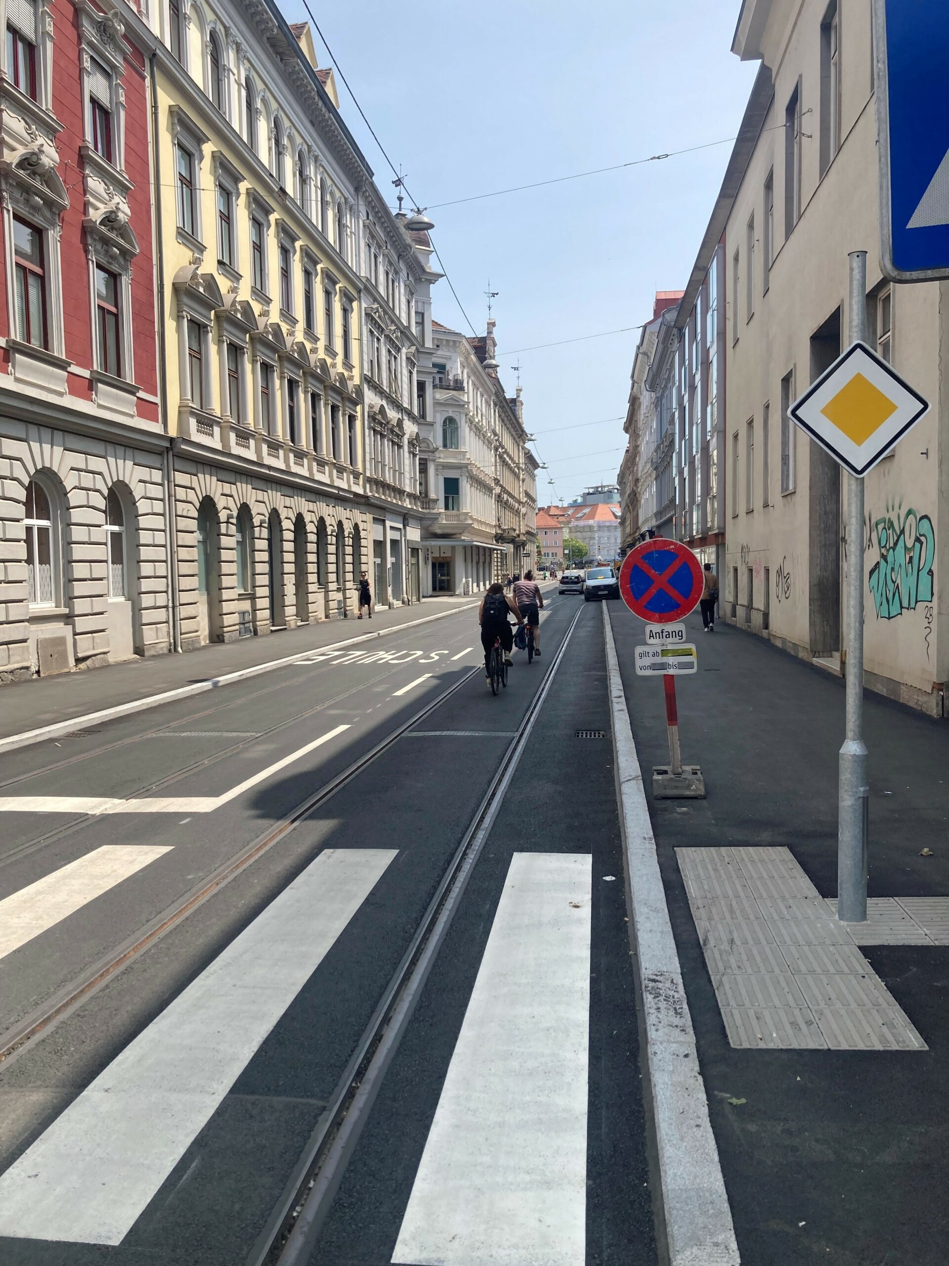 Eine Straßenansicht von Graz mit Radfahrern und Straßenschildern.